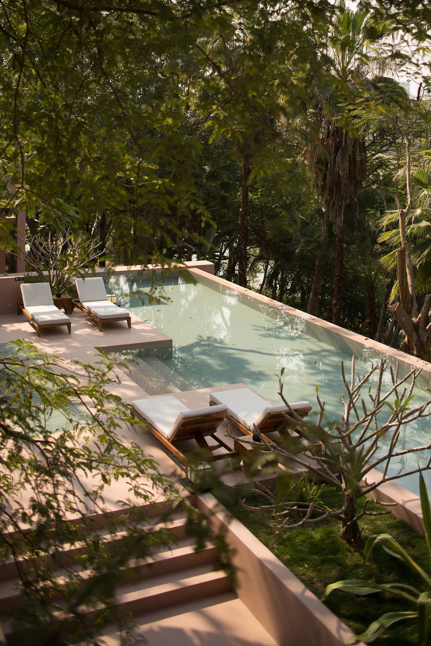 A serene outdoor pool surrounded by lush greenery and two white sun loungers, inviting relaxation and tranquility. A serene outdoor pool surrounded by lush greenery and two white sun loungers, inviting relaxation and tranquility.