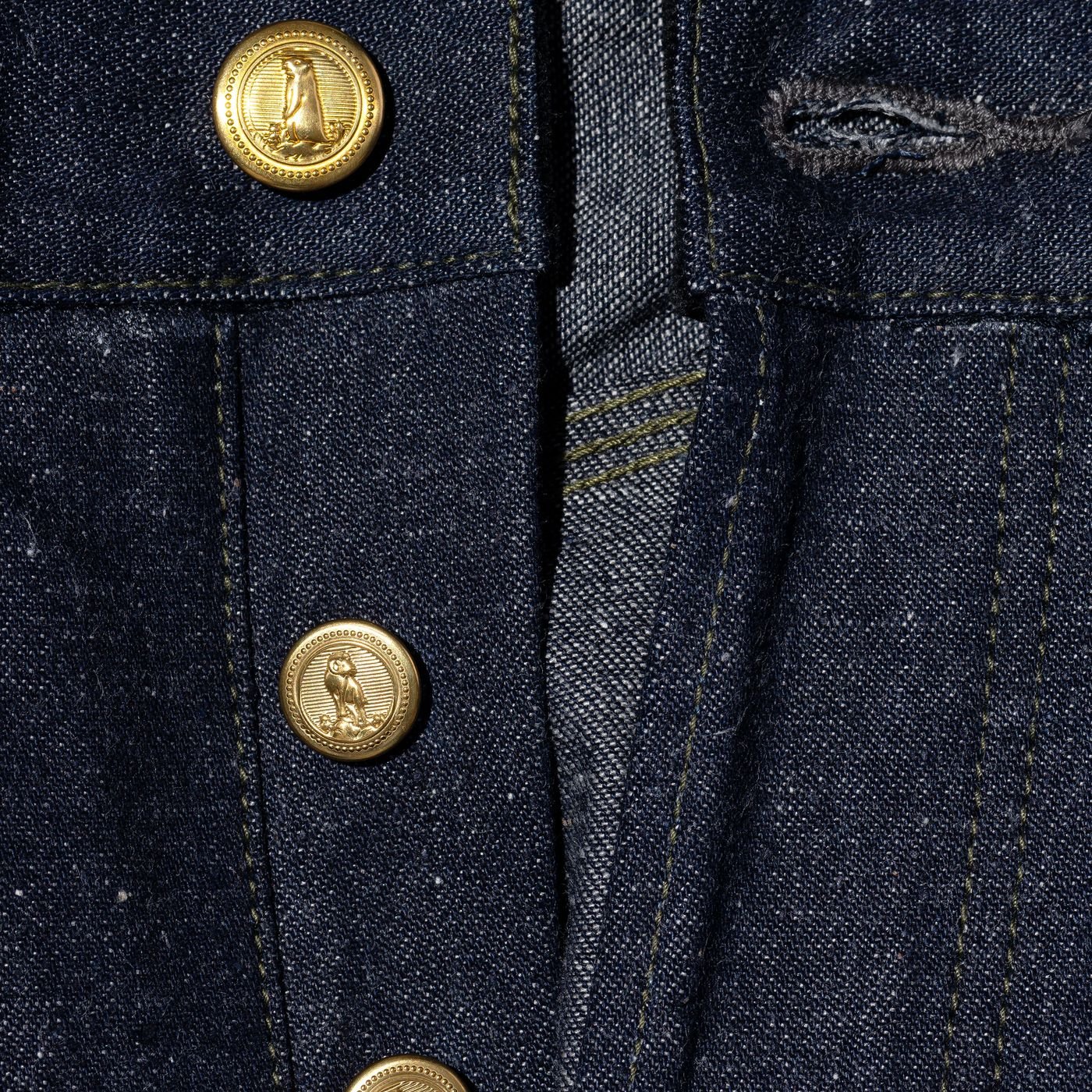 Close-up of a dark denim jacket featuring gold buttons with a penguin emblem.
