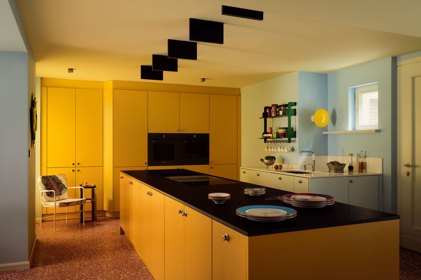 Modern kitchen featuring bright yellow cabinetry, a black island, colorful dishware, and a stylish blue accent wall. Modern kitchen featuring bright yellow cabinetry, a black island, colorful dishware, and a stylish blue accent wall.