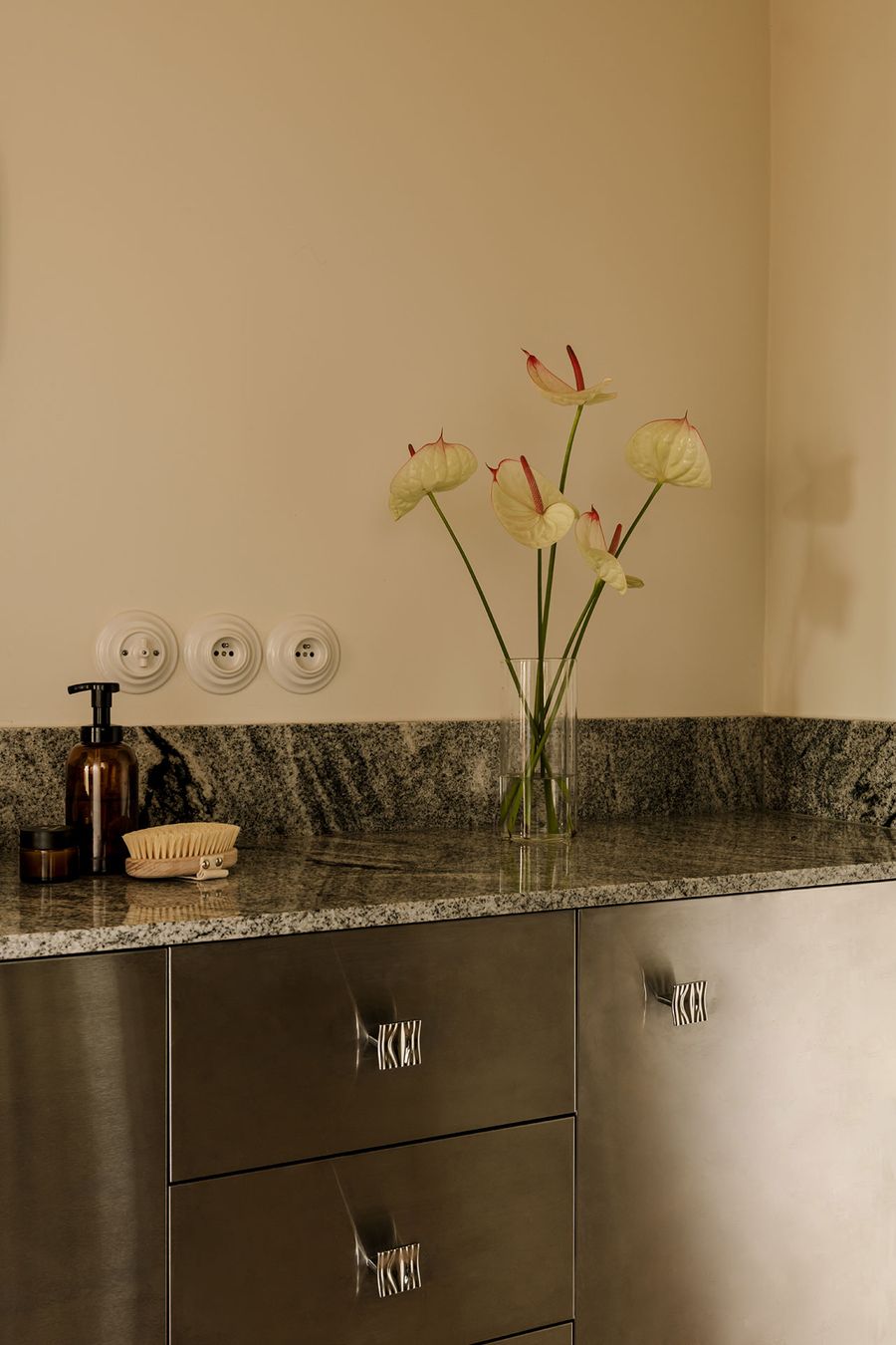 A sleek bathroom counter with a granite surface, steel cabinets, elegant flower vase, and skincare products arranged aesthetically. A sleek bathroom counter with a granite surface, steel cabinets, elegant flower vase, and skincare products arranged aesthetically.