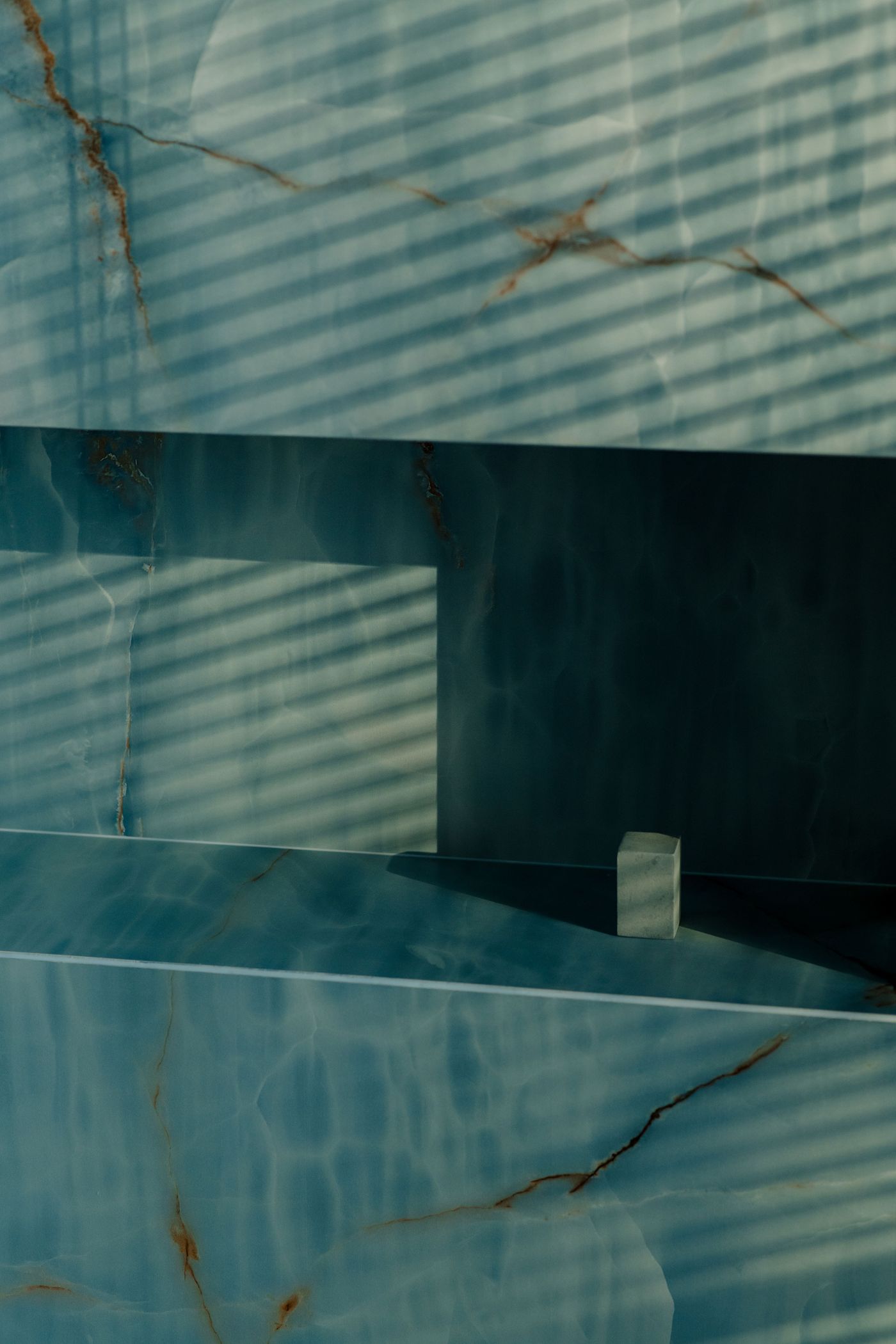 A detail of the blue onyx wall reveals its ethereal translucency and amber veining, enhanced by diagonal shadows from window blinds—capturing the space’s poetic balance of materiality and light.