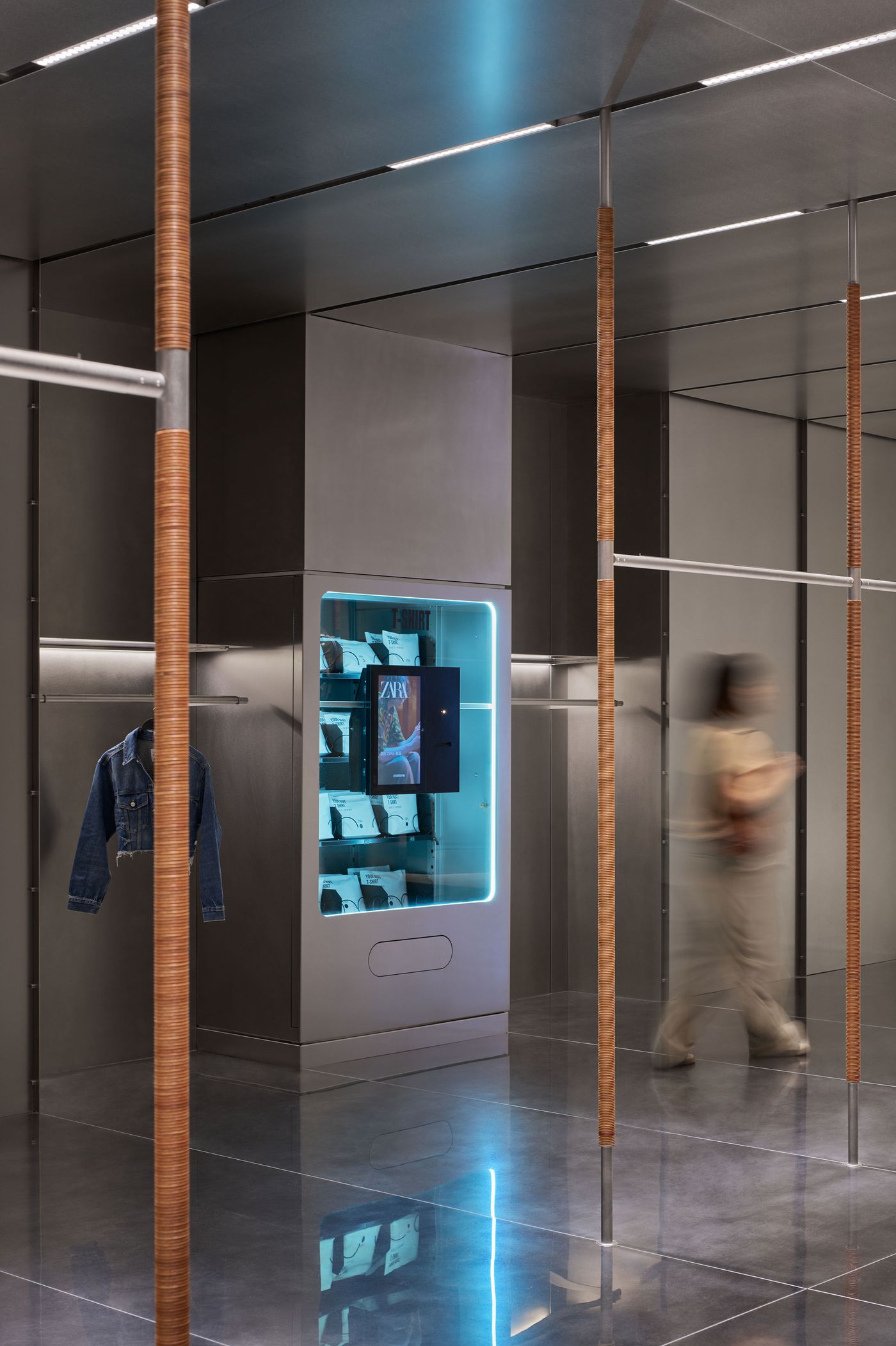 A modern retail space featuring a sleek vending machine showcasing clothing, with a blurred figure walking past.
