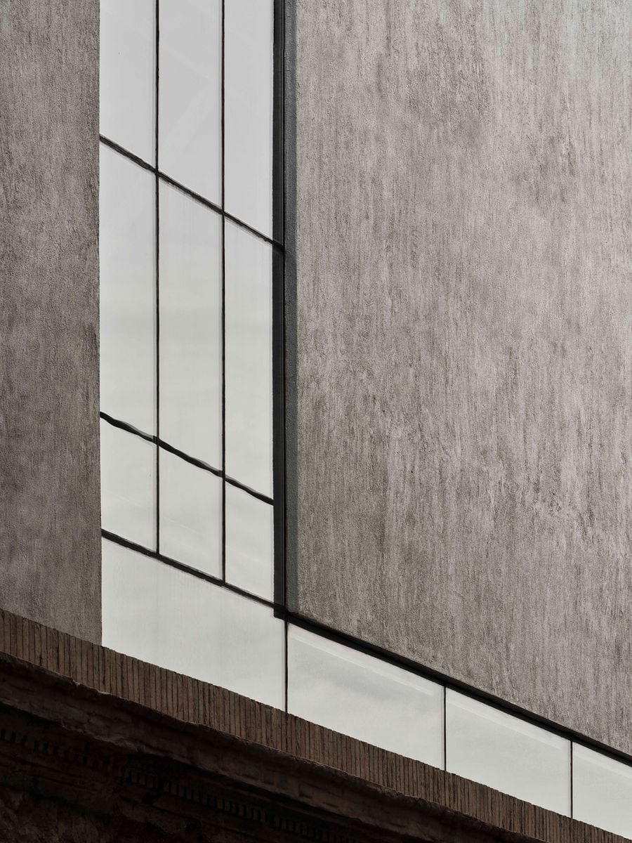 Vertical and horizontal glazing meet across the textured façade of Castor Place’s upper addition, breaking the otherwise monolithic volume into an asymmetrical composition. The clean window geometry contrasts with the deeply weathered brickwork and masonry visible along the retained building edge below. Vertical and horizontal glazing meet across the textured façade of Castor Place’s upper addition, breaking the otherwise monolithic volume into an asymmetrical composition. The clean window geometry contrasts with the deeply weathered brickwork and masonry visible along the retained building edge below.