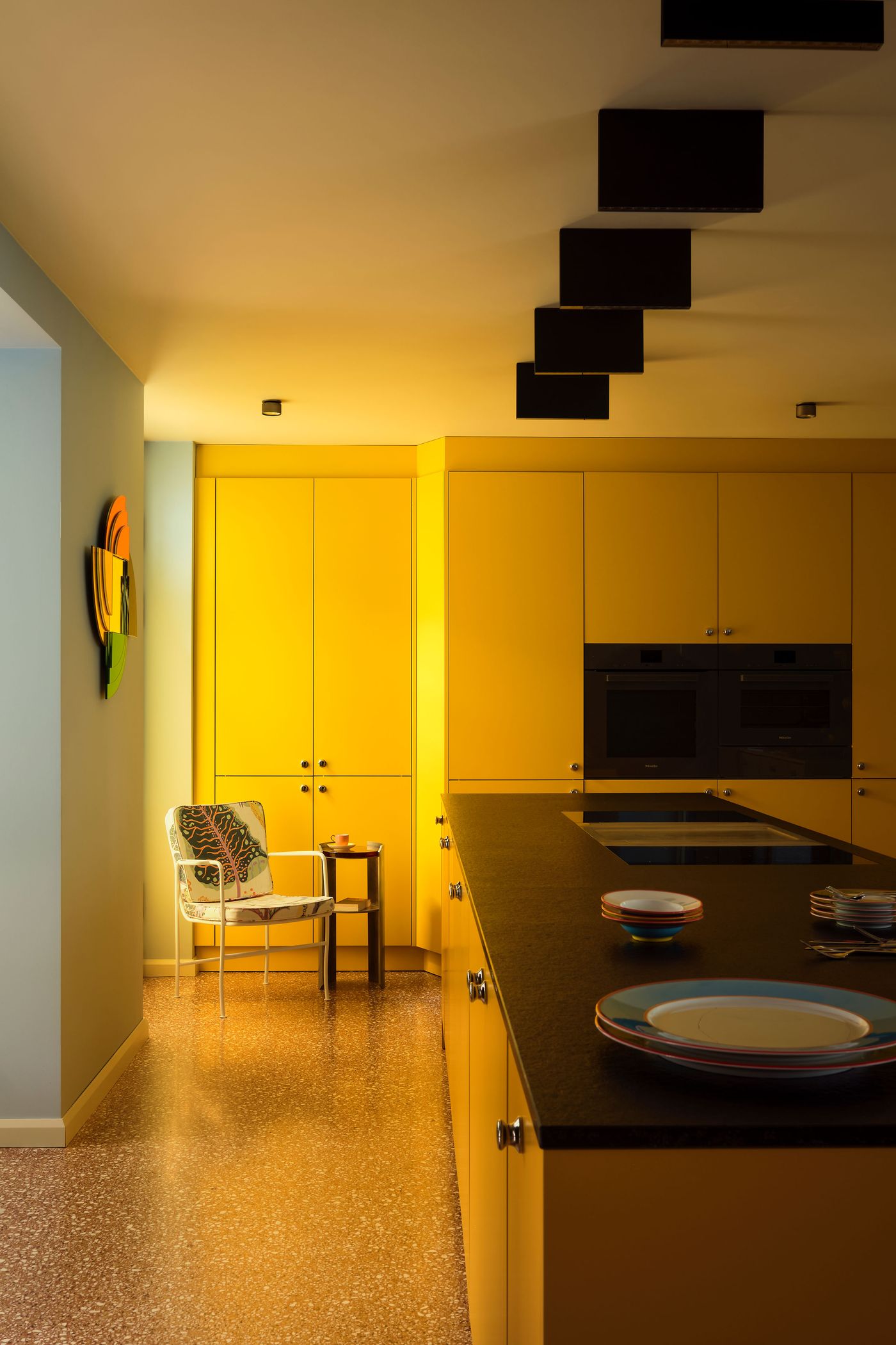 Bright yellow kitchen with sleek cabinets, a dark countertop, and a stylish chair beside a small table, creating a warm ambiance. Bright yellow kitchen with sleek cabinets, a dark countertop, and a stylish chair beside a small table, creating a warm ambiance.