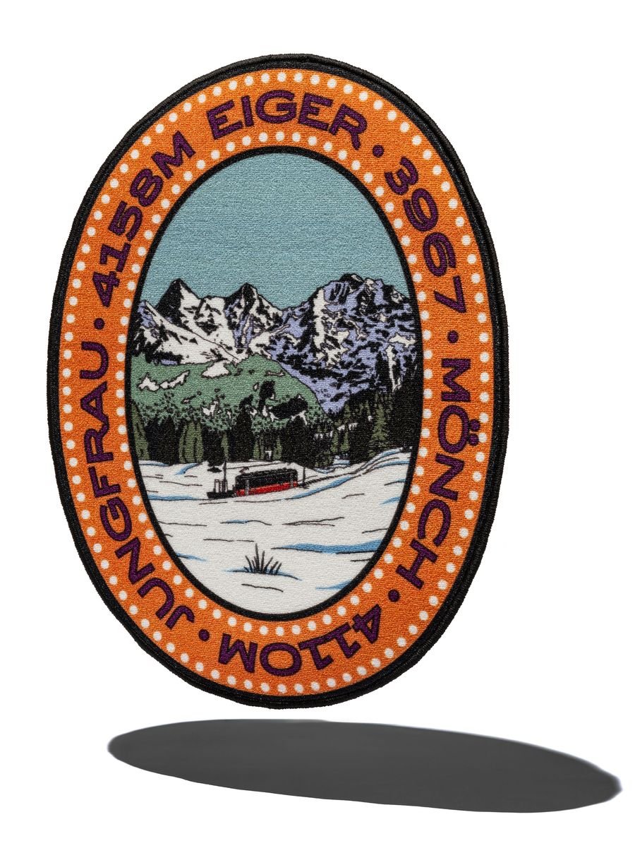 Colorful rug featuring snow-capped mountains and a red train, labeled with "Jungfrau," "Eiger," and "Mönch" altitudes in meters.