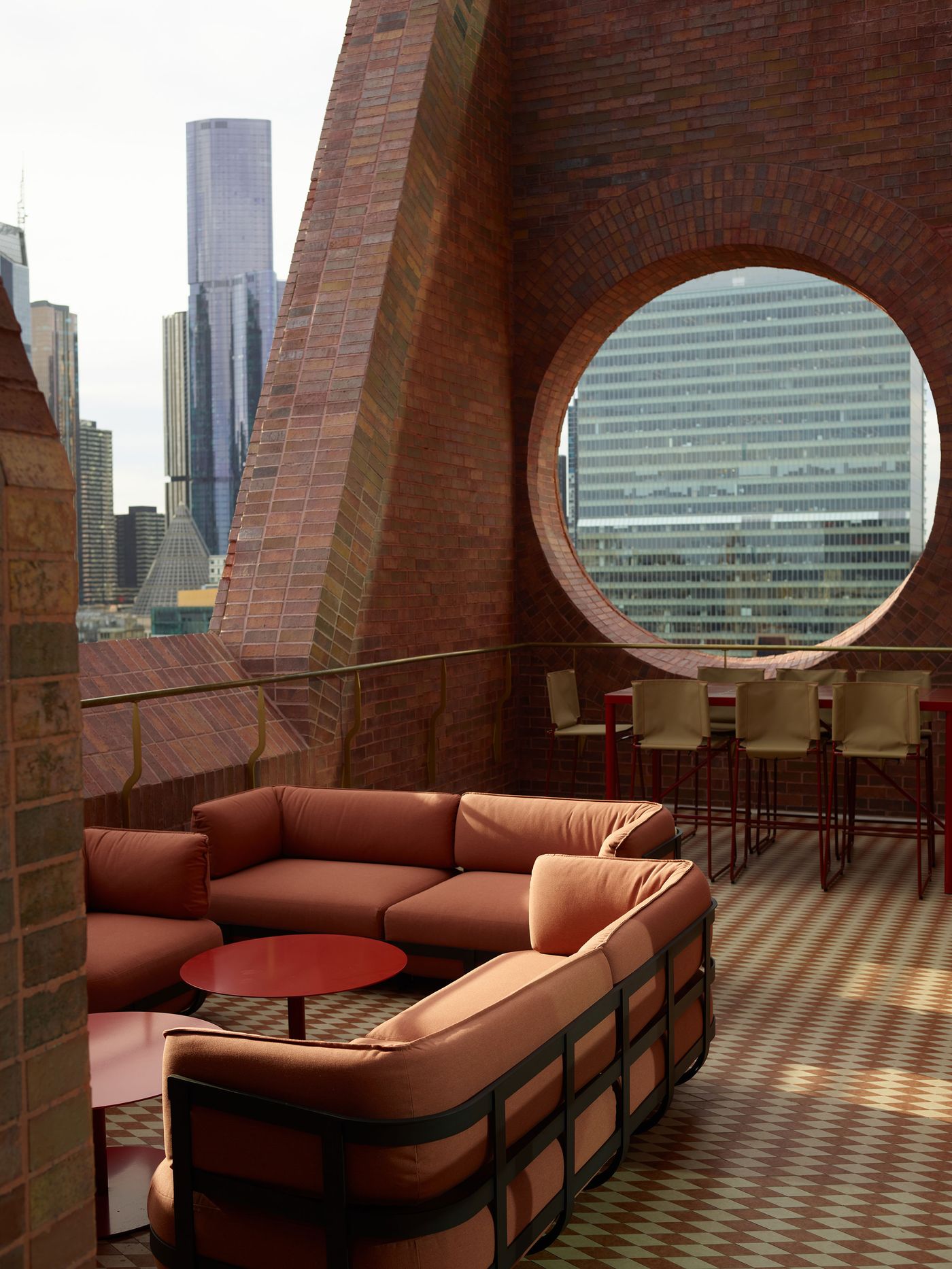A modern rooftop lounge features a circular brick window, stylish seating, and a view of skyscrapers in the background. A modern rooftop lounge features a circular brick window, stylish seating, and a view of skyscrapers in the background.