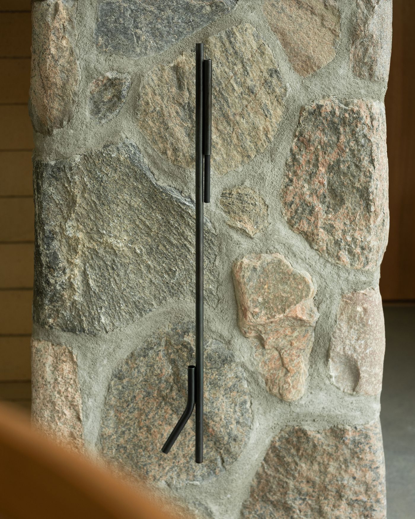 A minimalist black metal handle mounted on a textured stone wall, contrasting with the natural stone textures and colors.