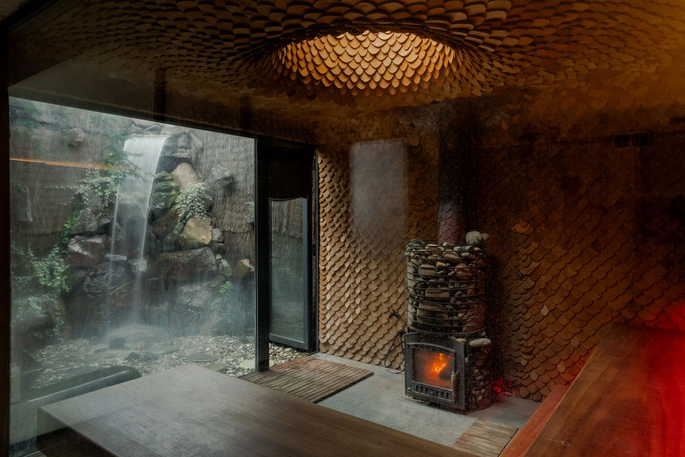 Cozy interior featuring a stone fireplace, unique scale-patterned walls, and a view of a serene waterfall through glass. Cozy interior featuring a stone fireplace, unique scale-patterned walls, and a view of a serene waterfall through glass.