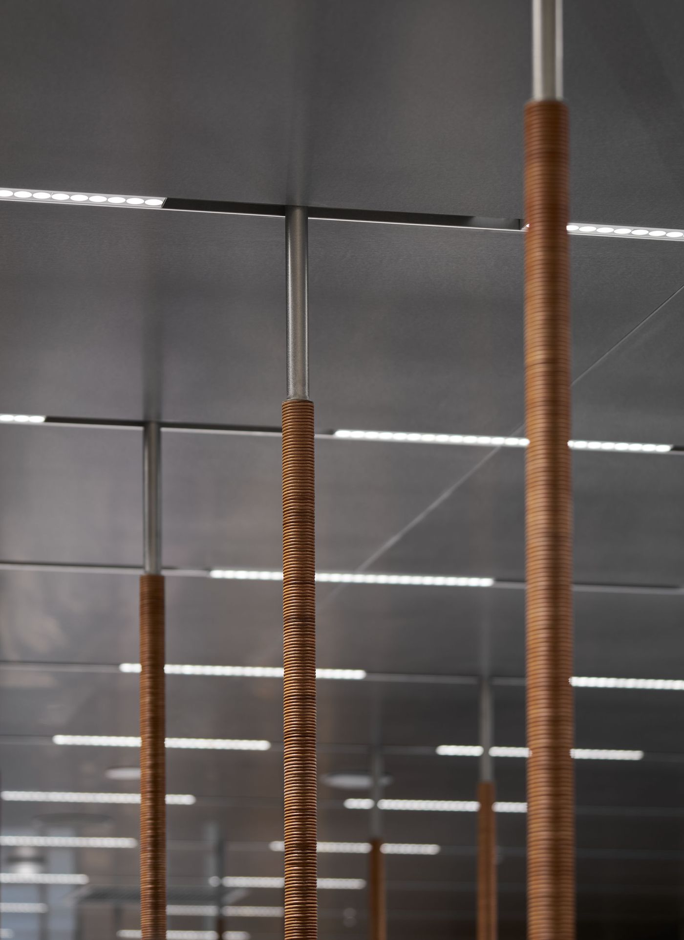 Three poles with twisted brown grips against a modern ceiling featuring bright, recessed lighting.