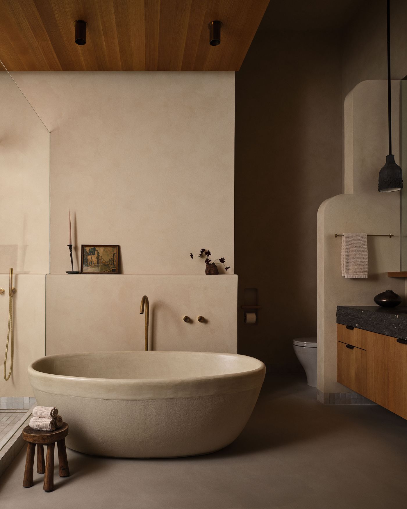 A minimalist bathroom featuring a freestanding stone bathtub, wooden ceiling, warm tones, and elegant fixtures with decorative accents.