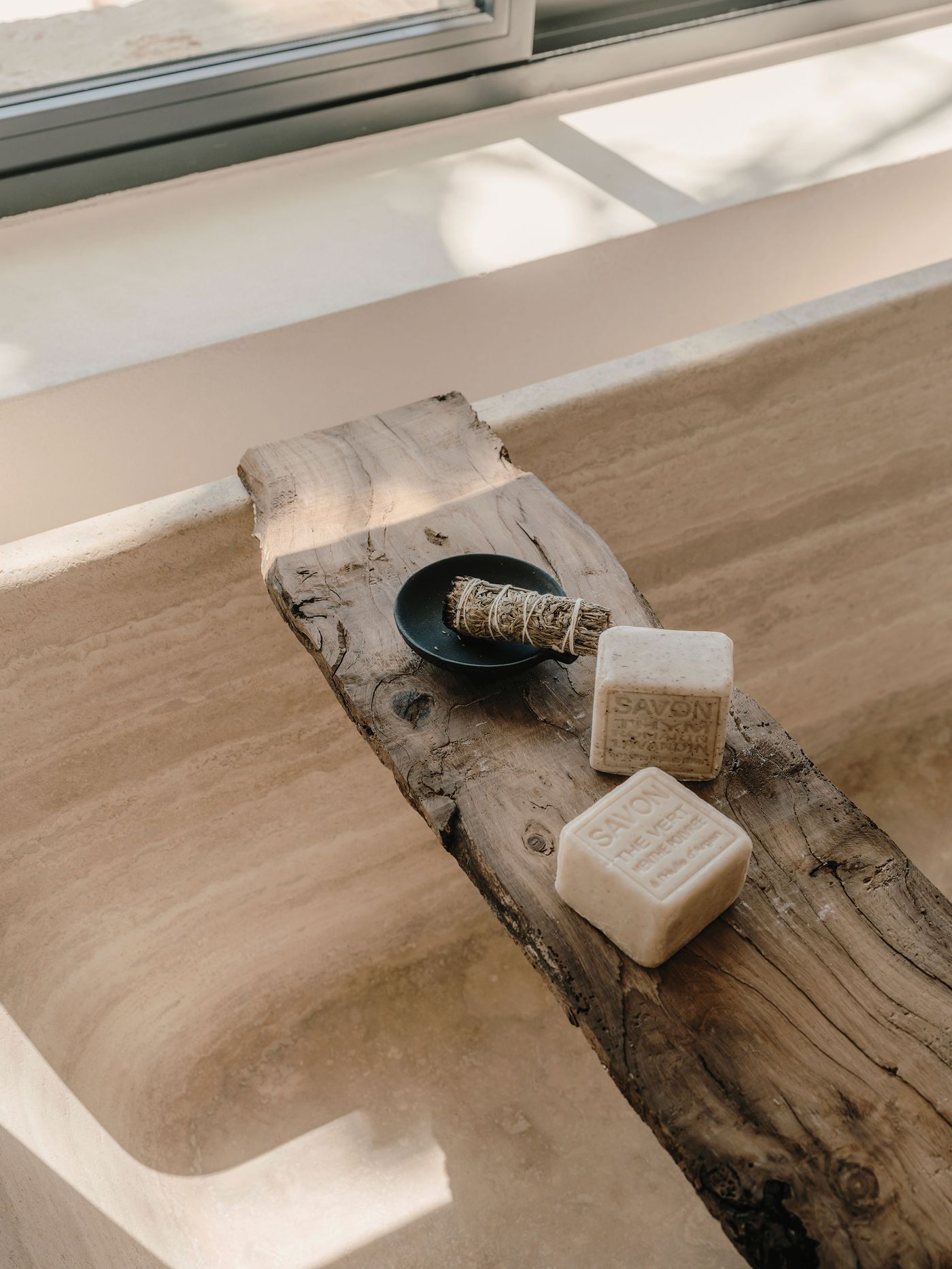 A wooden shelf displays two artisanal soaps and a bundle of herbs, set against a light, minimalist bathroom scene. A wooden shelf displays two artisanal soaps and a bundle of herbs, set against a light, minimalist bathroom scene.
