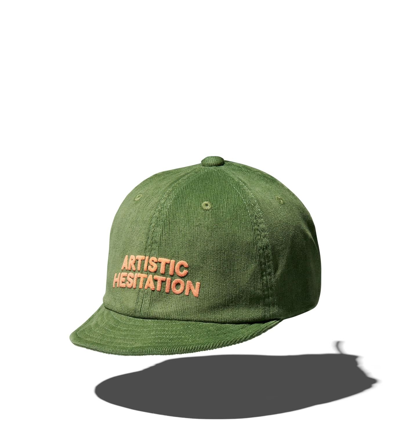 Olive green cap with "ARTISTIC HESITATION" stitched in peach, floating against a white background, casting a soft shadow.