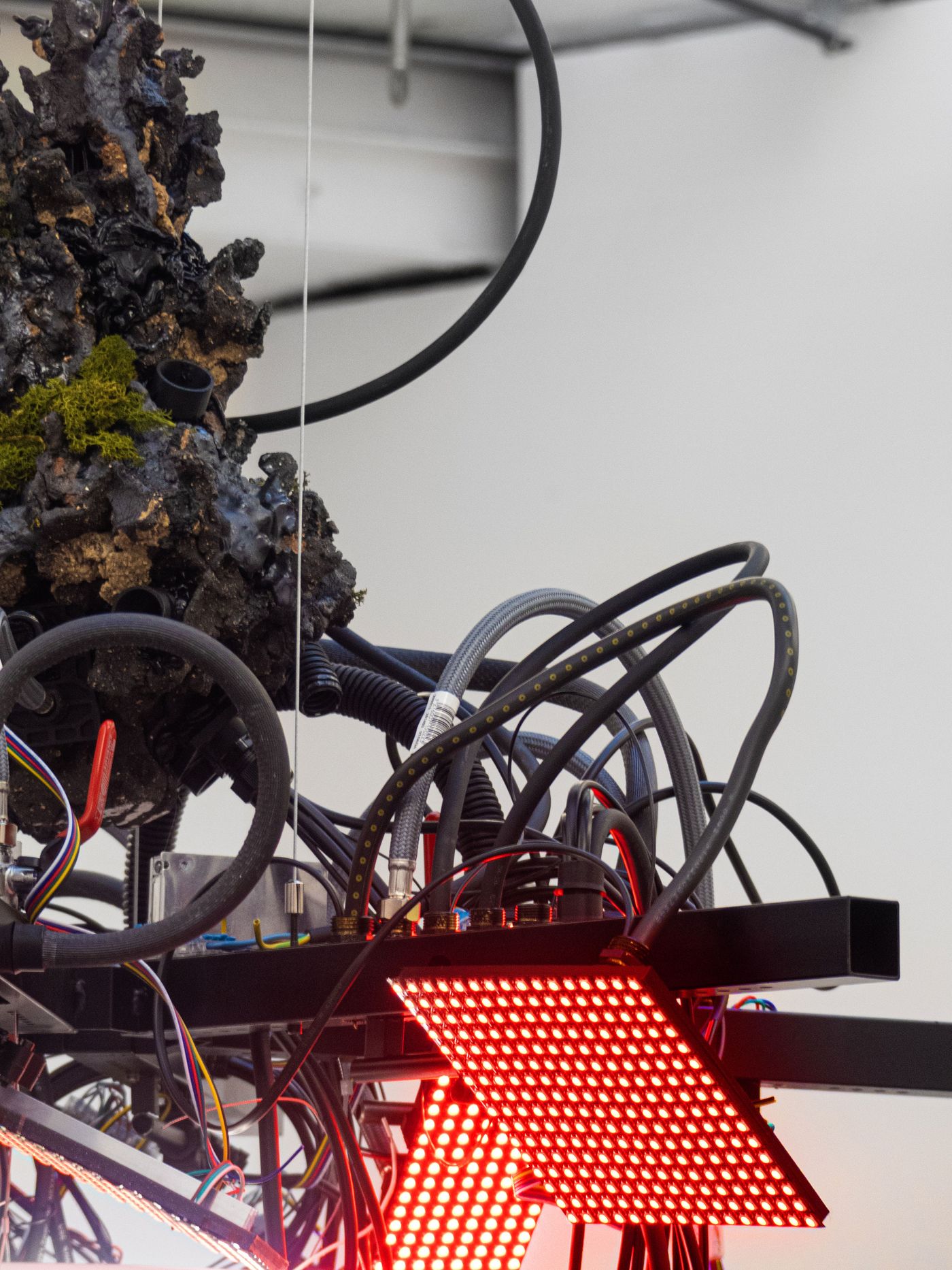 An abstract assembly featuring rocky textures, green moss, and numerous cables alongside illuminated red LED panels. An abstract assembly featuring rocky textures, green moss, and numerous cables alongside illuminated red LED panels.