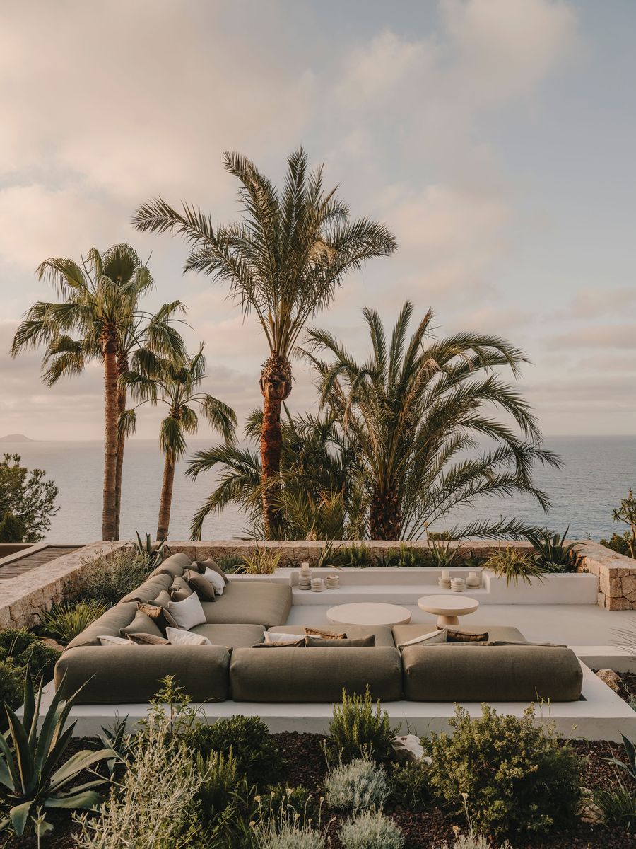 Luxurious outdoor lounge with a large green sectional, coffee table, and palms, overlooking the ocean under a soft sunset sky. Luxurious outdoor lounge with a large green sectional, coffee table, and palms, overlooking the ocean under a soft sunset sky.