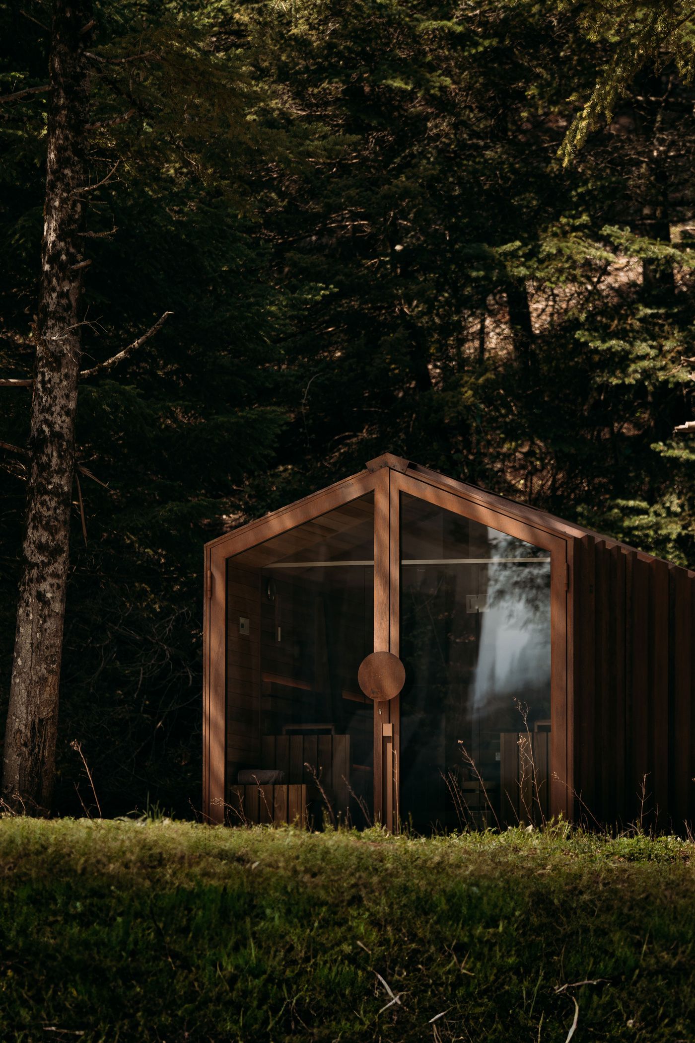A contemporary, minimalist sauna cabin with a full glass front and warm wooden construction is subtly positioned within a natural forest setting. The transparent facade offers views of the surrounding trees, emphasizing a biophilic design that invites users to connect with nature while enjoying a restorative experience. A contemporary, minimalist sauna cabin with a full glass front and warm wooden construction is subtly positioned within a natural forest setting. The transparent facade offers views of the surrounding trees, emphasizing a biophilic design that invites users to connect with nature while enjoying a restorative experience.