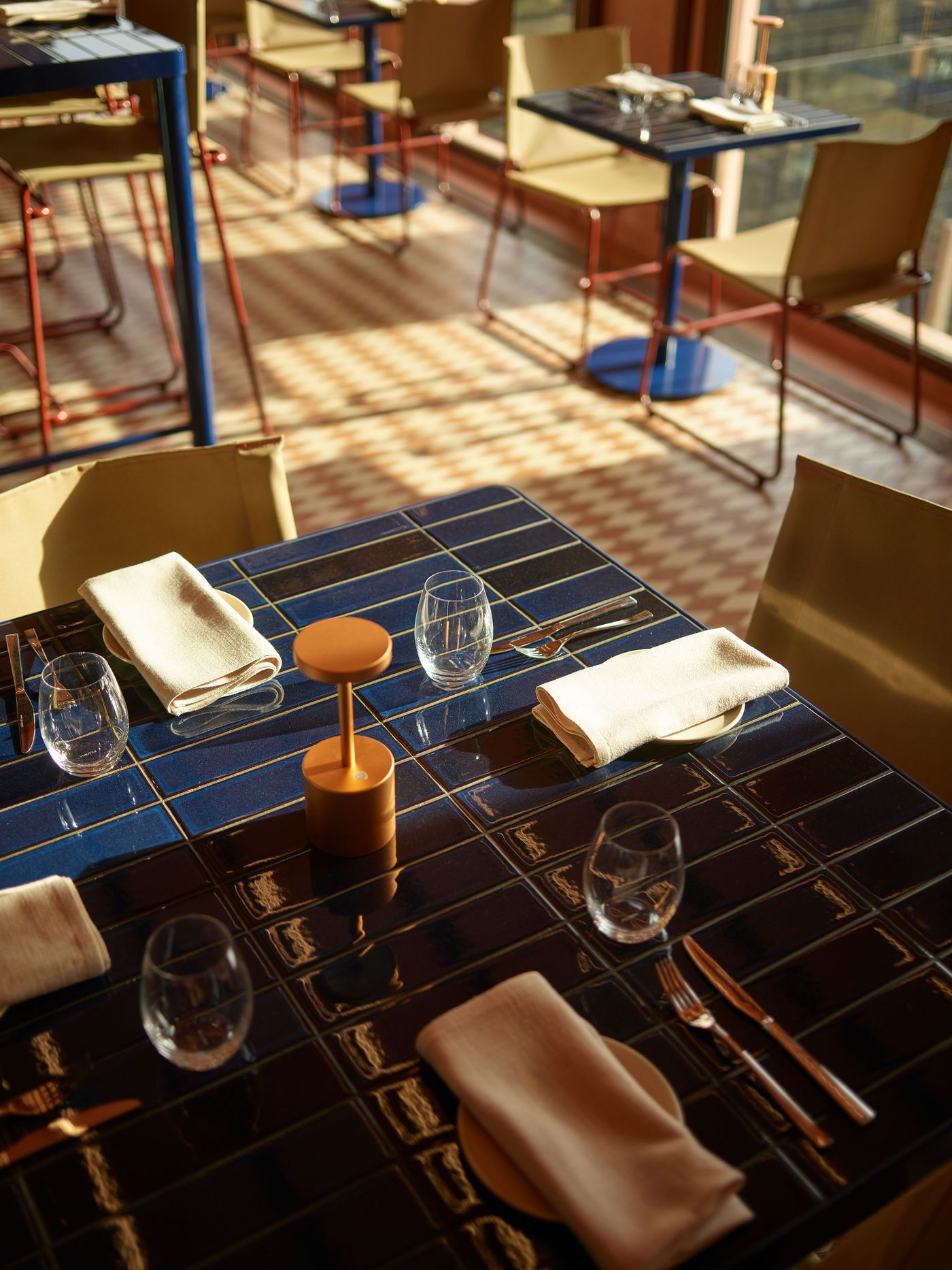 A brightly lit restaurant table set with blue tiled surface, folded napkins, glassware, and a decorative centerpiece. A brightly lit restaurant table set with blue tiled surface, folded napkins, glassware, and a decorative centerpiece.