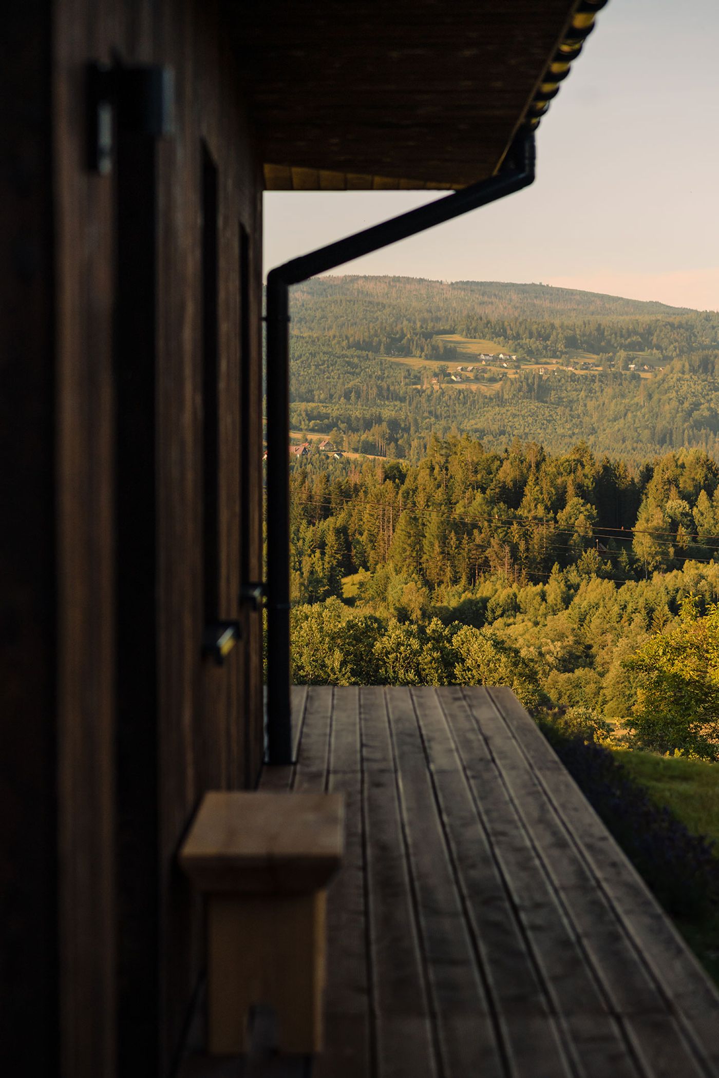A wooden deck with a railing overlooks dense green forests and hills in warm evening light, creating a serene natural landscape. A wooden deck with a railing overlooks dense green forests and hills in warm evening light, creating a serene natural landscape.