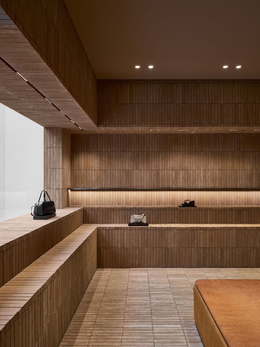 A minimalist interior featuring textured brown walls and shelving, displaying stylish handbags in a warm, softly lit space. A minimalist interior featuring textured brown walls and shelving, displaying stylish handbags in a warm, softly lit space.