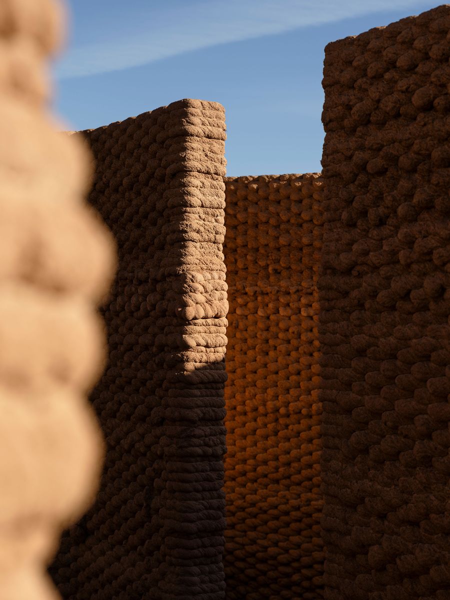 Two textured clay walls create a narrow passageway, illuminated by natural light against a clear blue sky. Two textured clay walls create a narrow passageway, illuminated by natural light against a clear blue sky.