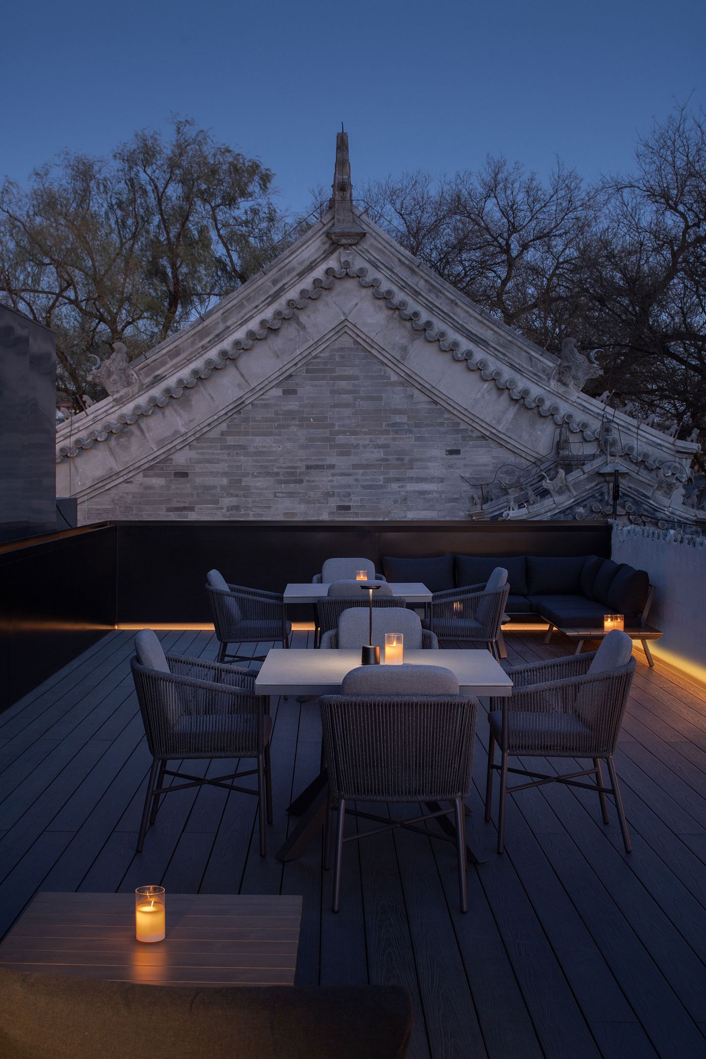 A serene rooftop terrace with modern furniture and soft candlelight, framed by the traditional roof of an ancient building at twilight. A serene rooftop terrace with modern furniture and soft candlelight, framed by the traditional roof of an ancient building at twilight.