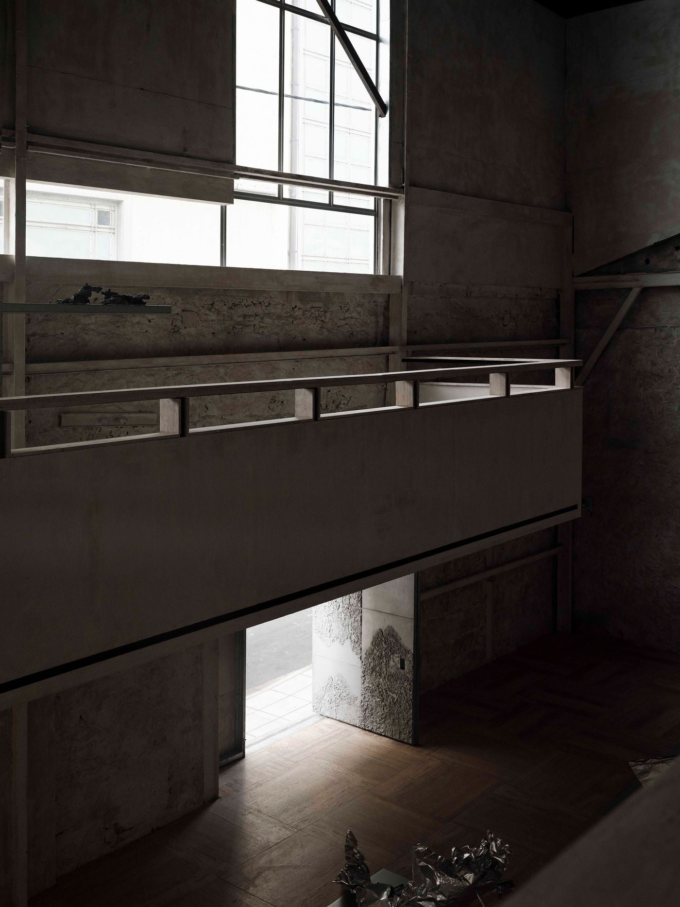 A suspended walkway crosses the double-height gallery, silhouetted against tall windows and rough masonry walls. Daylight entering through the entrance below creates a bright threshold within the otherwise shadowy interior, emphasising the vertical connections and layered circulation that define Castor Place. A suspended walkway crosses the double-height gallery, silhouetted against tall windows and rough masonry walls. Daylight entering through the entrance below creates a bright threshold within the otherwise shadowy interior, emphasising the vertical connections and layered circulation that define Castor Place.