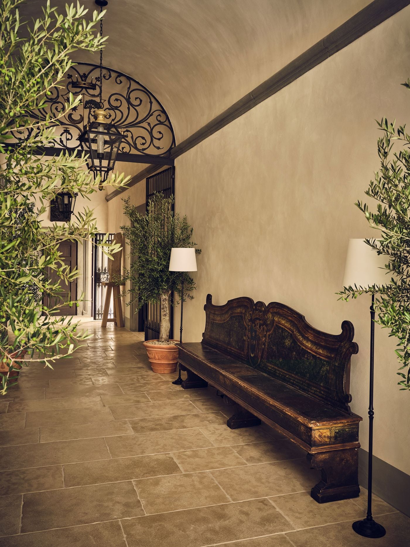 A barrel-vaulted entrance passage at La Réserve Firenze, paved in worn stone flags and lined with olive trees in terracotta pots. An antique bench with a carved, scrolling painted back rests against the wall, while glazed lanterns hang before a wrought-iron lunette and gate leading deeper into the palazzo. A barrel-vaulted entrance passage at La Réserve Firenze, paved in worn stone flags and lined with olive trees in terracotta pots. An antique bench with a carved, scrolling painted back rests against the wall, while glazed lanterns hang before a wrought-iron lunette and gate leading deeper into the palazzo.