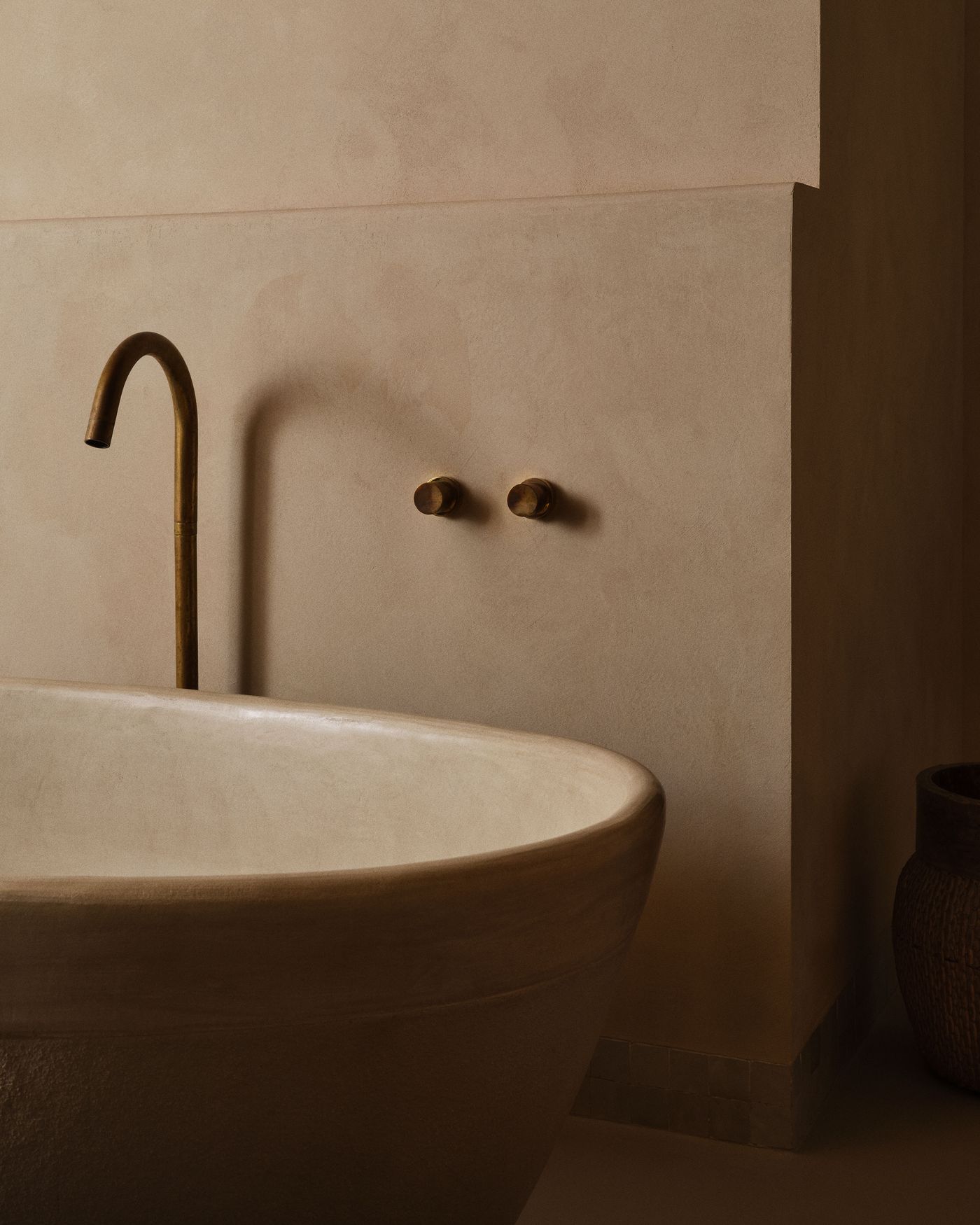 A serene bathroom scene featuring a curved stone bathtub, a sleek brass faucet, and minimalist, warm-toned walls.
