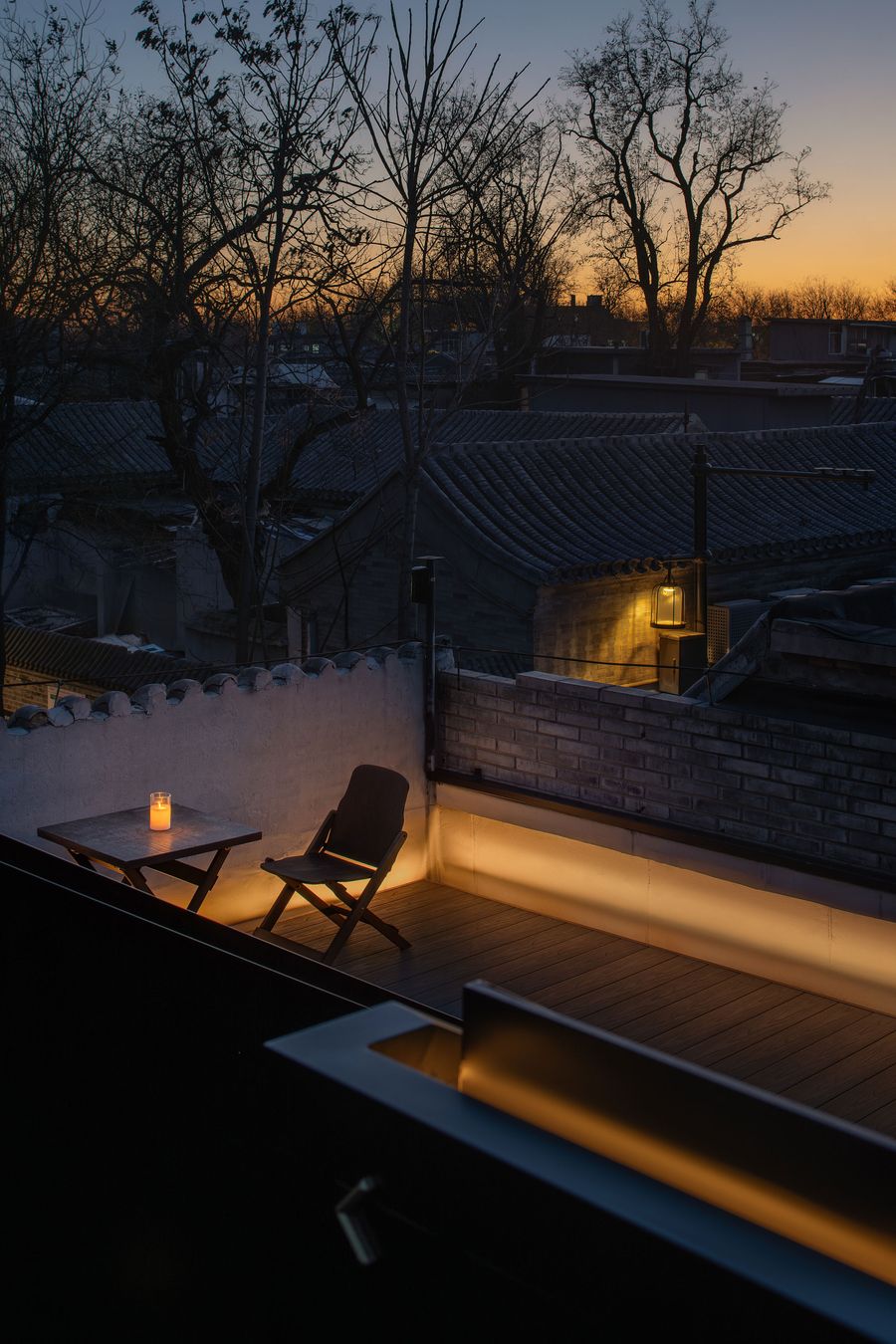 A cozy rooftop terrace at dusk, featuring a candlelit table and chair, with glowing lights against a backdrop of silhouetted trees and rooftops. A cozy rooftop terrace at dusk, featuring a candlelit table and chair, with glowing lights against a backdrop of silhouetted trees and rooftops.