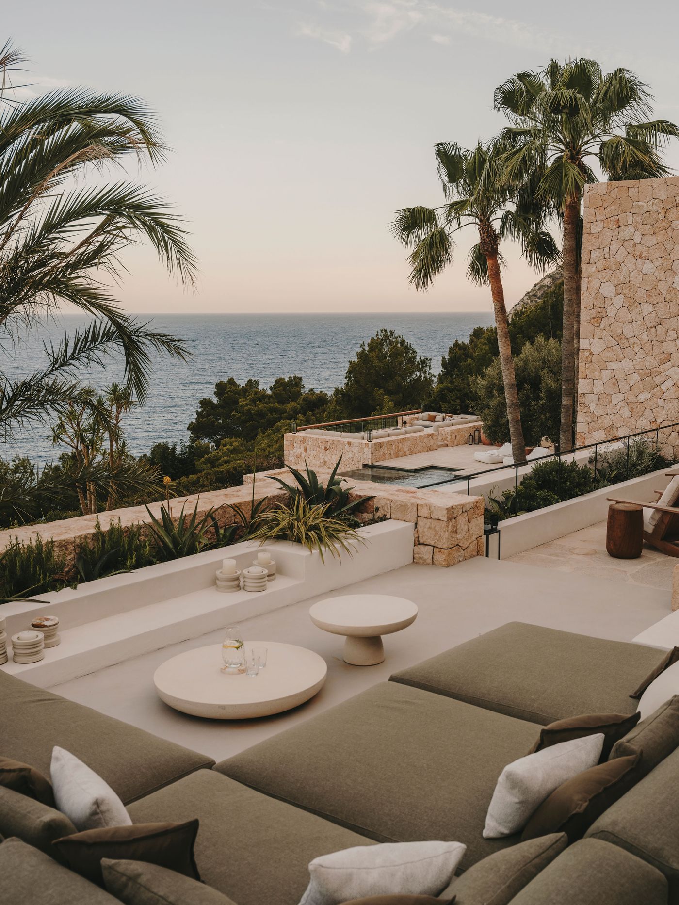 Luxury outdoor lounge area with plush seating, minimalist tables, and palm trees overlooking a serene ocean view at sunset. Luxury outdoor lounge area with plush seating, minimalist tables, and palm trees overlooking a serene ocean view at sunset.