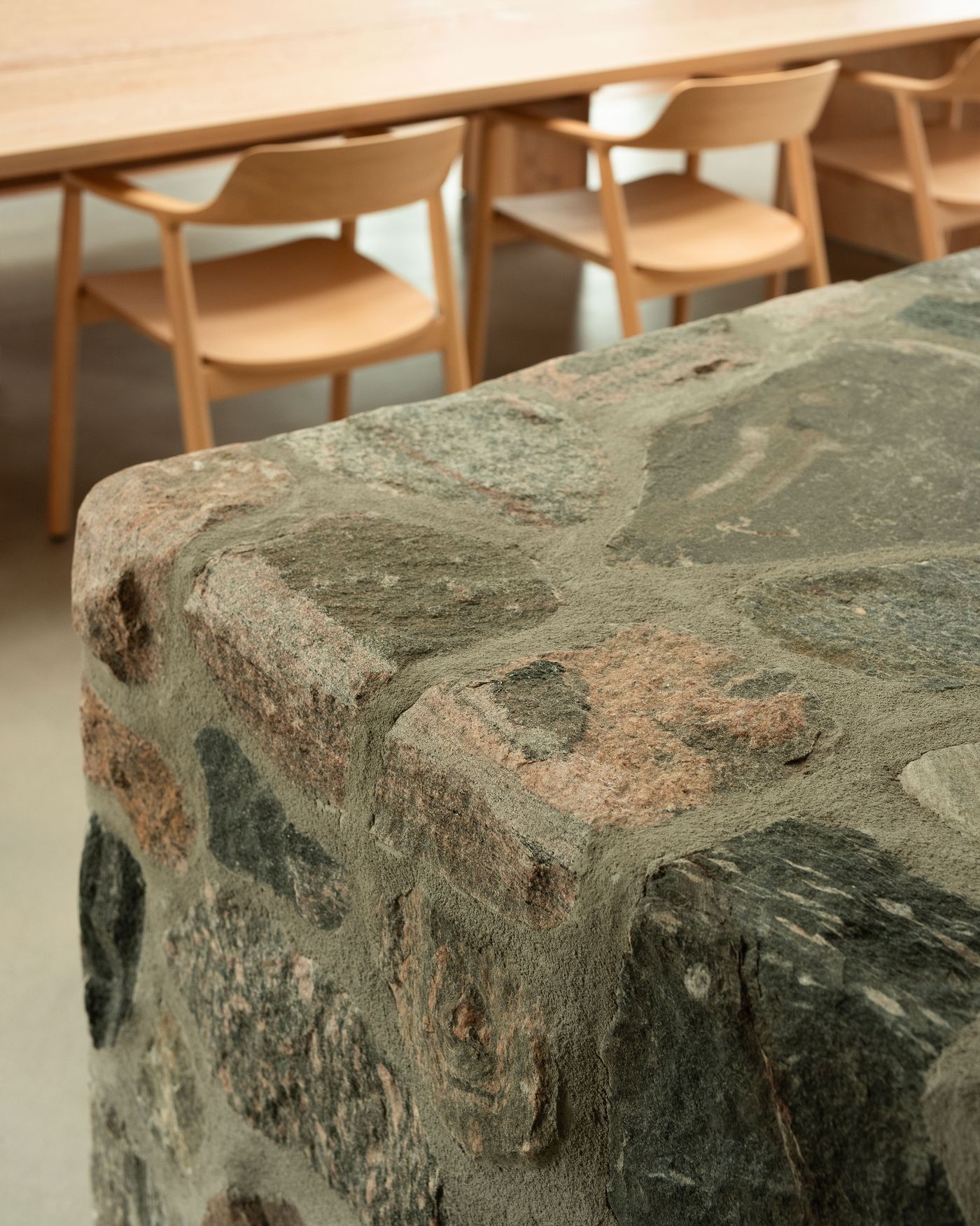 Close-up of a textured stone surface, with a wooden table and minimalist chairs softly blurred in the background.