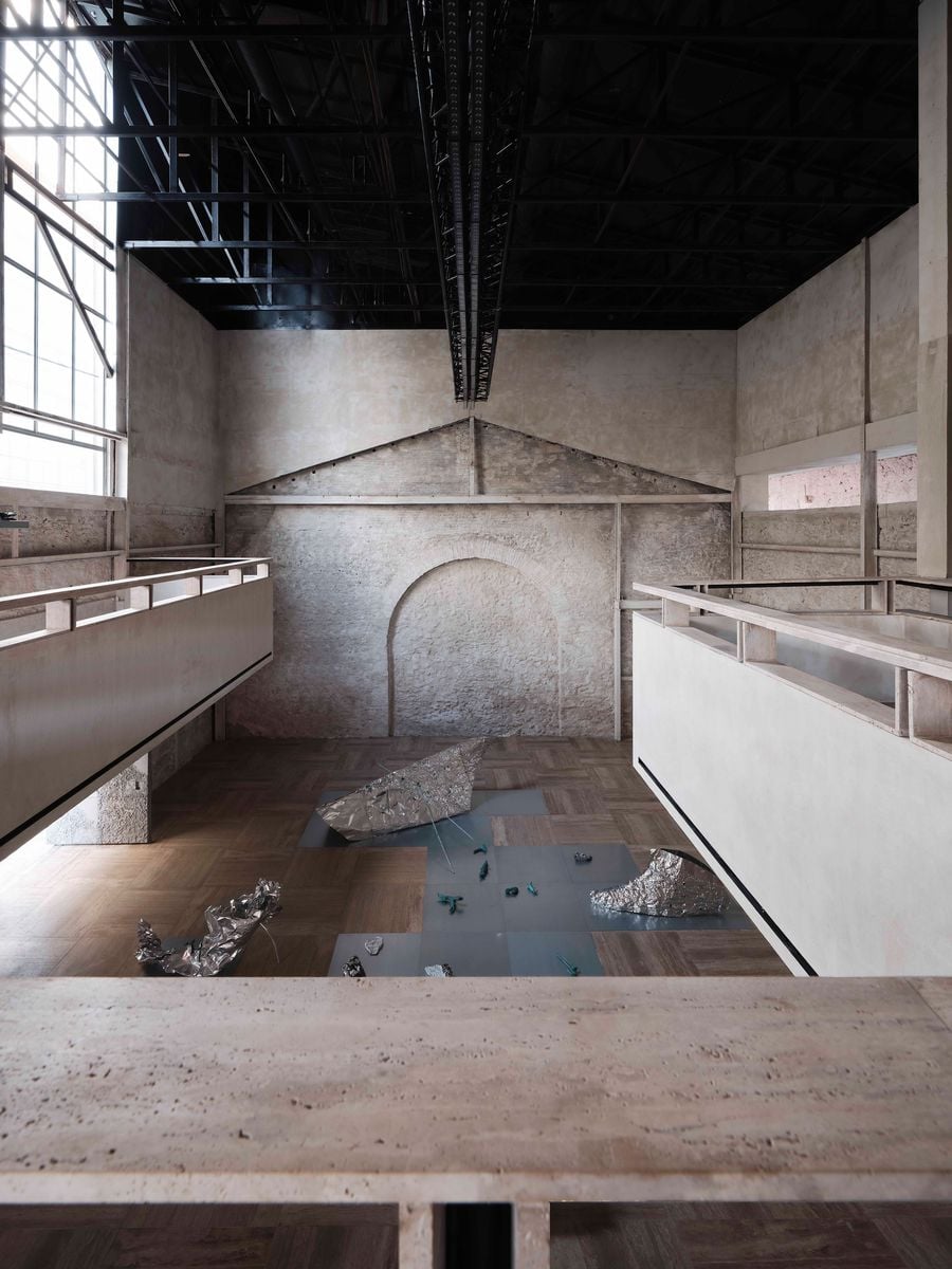 Seen from the upper-level walkway, Castor Place’s soaring central hall brings the building’s different eras into one frame: rough masonry, the ghostly outline of a former pitched roof, pale suspended galleries and a black steel roof structure. Sculptural works from the “Casting Water” exhibition punctuate the travertine floor below. Seen from the upper-level walkway, Castor Place’s soaring central hall brings the building’s different eras into one frame: rough masonry, the ghostly outline of a former pitched roof, pale suspended galleries and a black steel roof structure. Sculptural works from the “Casting Water” exhibition punctuate the travertine floor below.