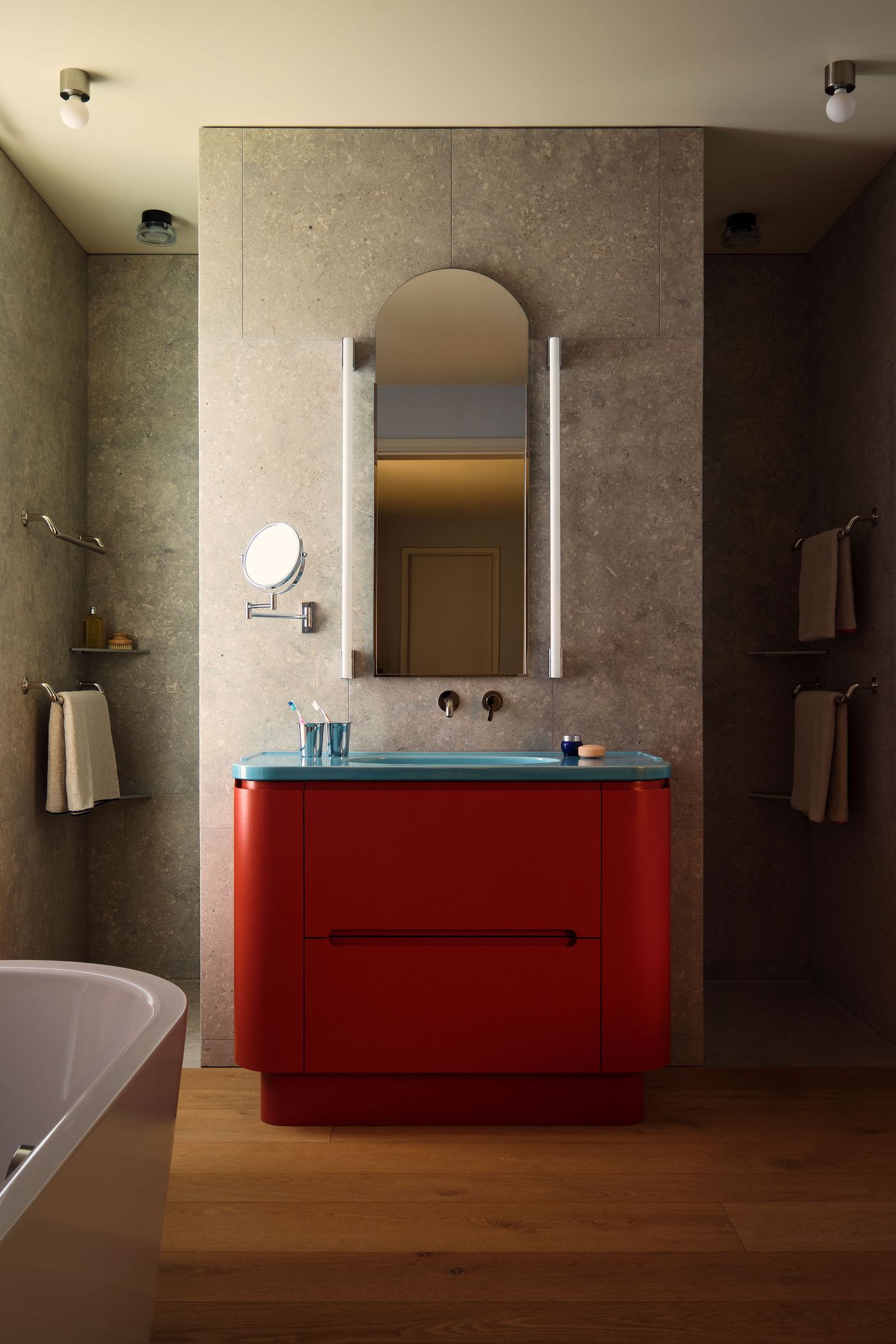 A modern bathroom featuring a striking red vanity with a blue countertop, a large mirror, sleek fixtures, and minimalist decor.