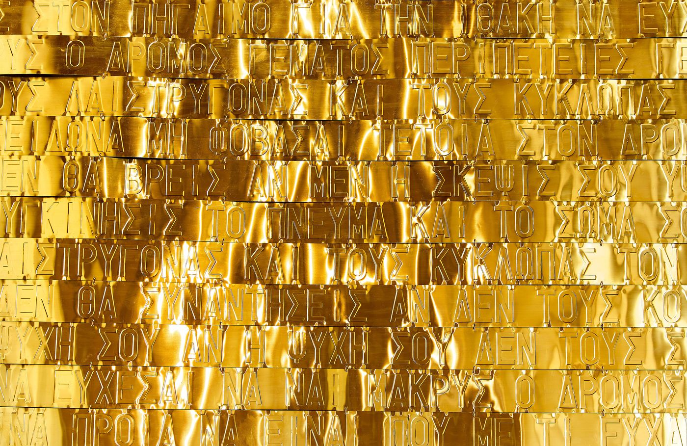 A close-up of a contemporary art piece by Gabriel Leger. The work features multiple horizontal rows of golden, rectangular metal sheets, each bearing carved Greek text. The surface reflects light, creating a textured, shimmering effect that blurs the lines between ancient inscription and modern abstraction. A close-up of a contemporary art piece by Gabriel Leger. The work features multiple horizontal rows of golden, rectangular metal sheets, each bearing carved Greek text. The surface reflects light, creating a textured, shimmering effect that blurs the lines between ancient inscription and modern abstraction.