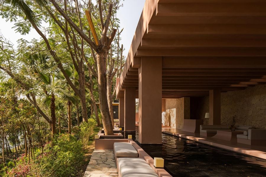 A modern, open-air living space featuring textured walls, smooth seating, and a tranquil water feature, surrounded by lush greenery.