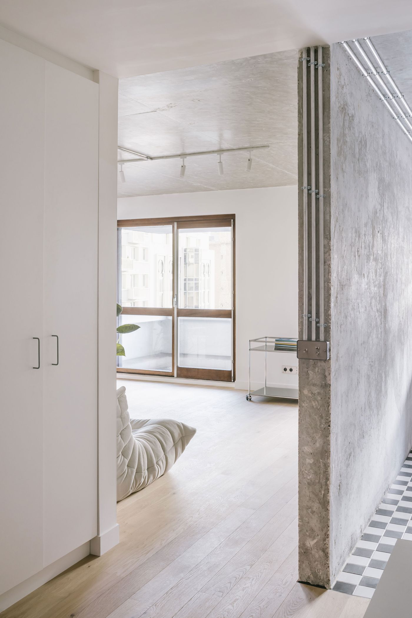 Modern interior view showcasing a cozy living area with a padded seat, large windows, and a mix of concrete and white walls. Modern interior view showcasing a cozy living area with a padded seat, large windows, and a mix of concrete and white walls.