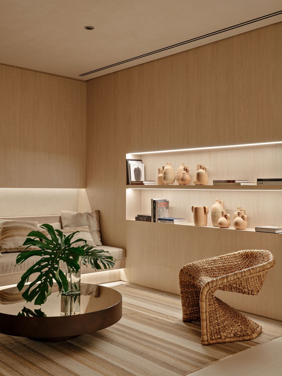An intimate corner of the lounge, showcasing a built-in banquette with warm, indirect lighting and a unique, sculptural rattan armchair. Recessed shelving displays artisanal ceramic vessels, reinforcing the space's focus on handcrafted details and a serene, Japandi-inspired aesthetic. An intimate corner of the lounge, showcasing a built-in banquette with warm, indirect lighting and a unique, sculptural rattan armchair. Recessed shelving displays artisanal ceramic vessels, reinforcing the space's focus on handcrafted details and a serene, Japandi-inspired aesthetic.