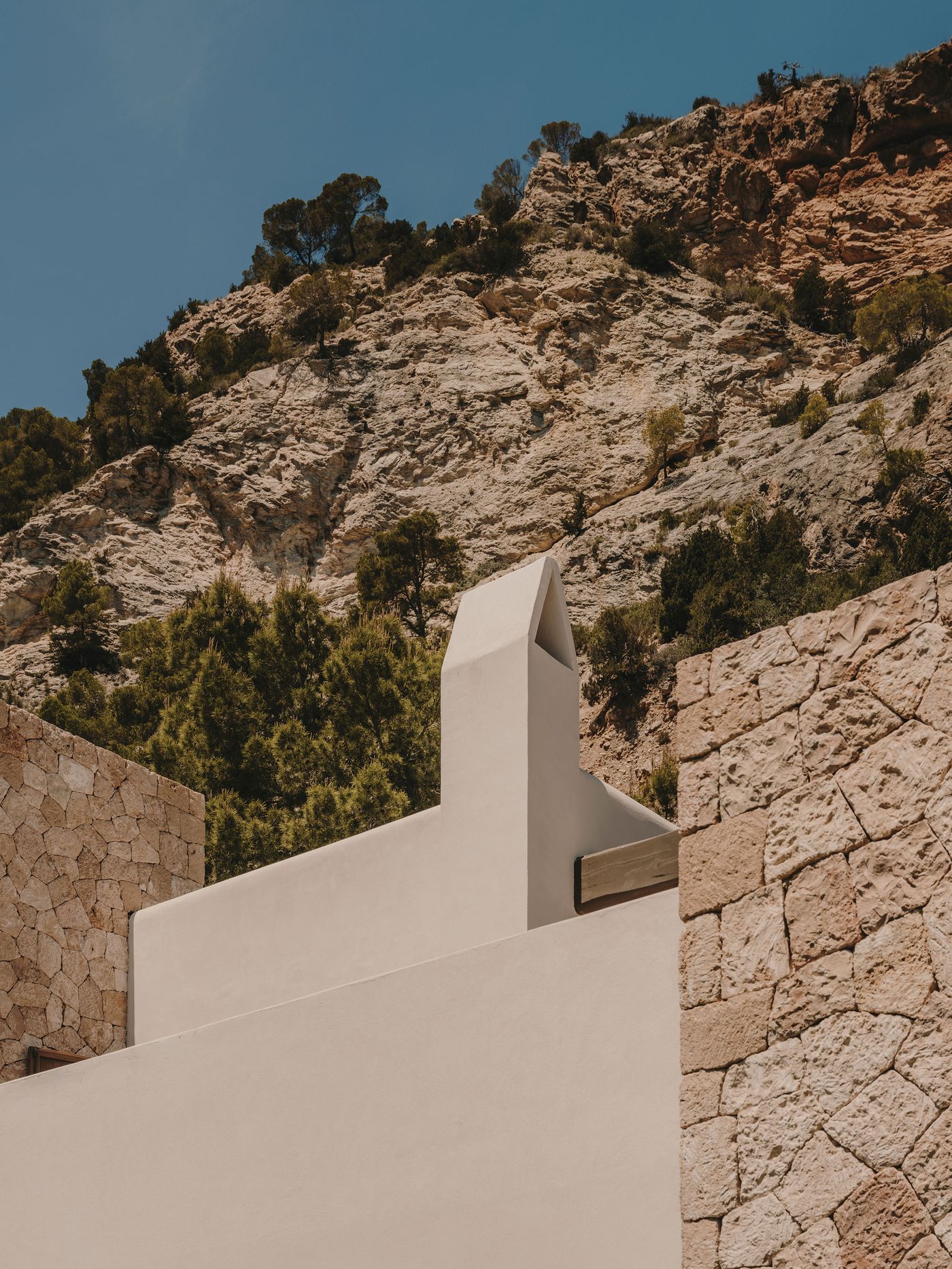 A minimalist white building contrasts with a rugged, rocky hillside under a clear blue sky, showcasing natural and architectural harmony. A minimalist white building contrasts with a rugged, rocky hillside under a clear blue sky, showcasing natural and architectural harmony.