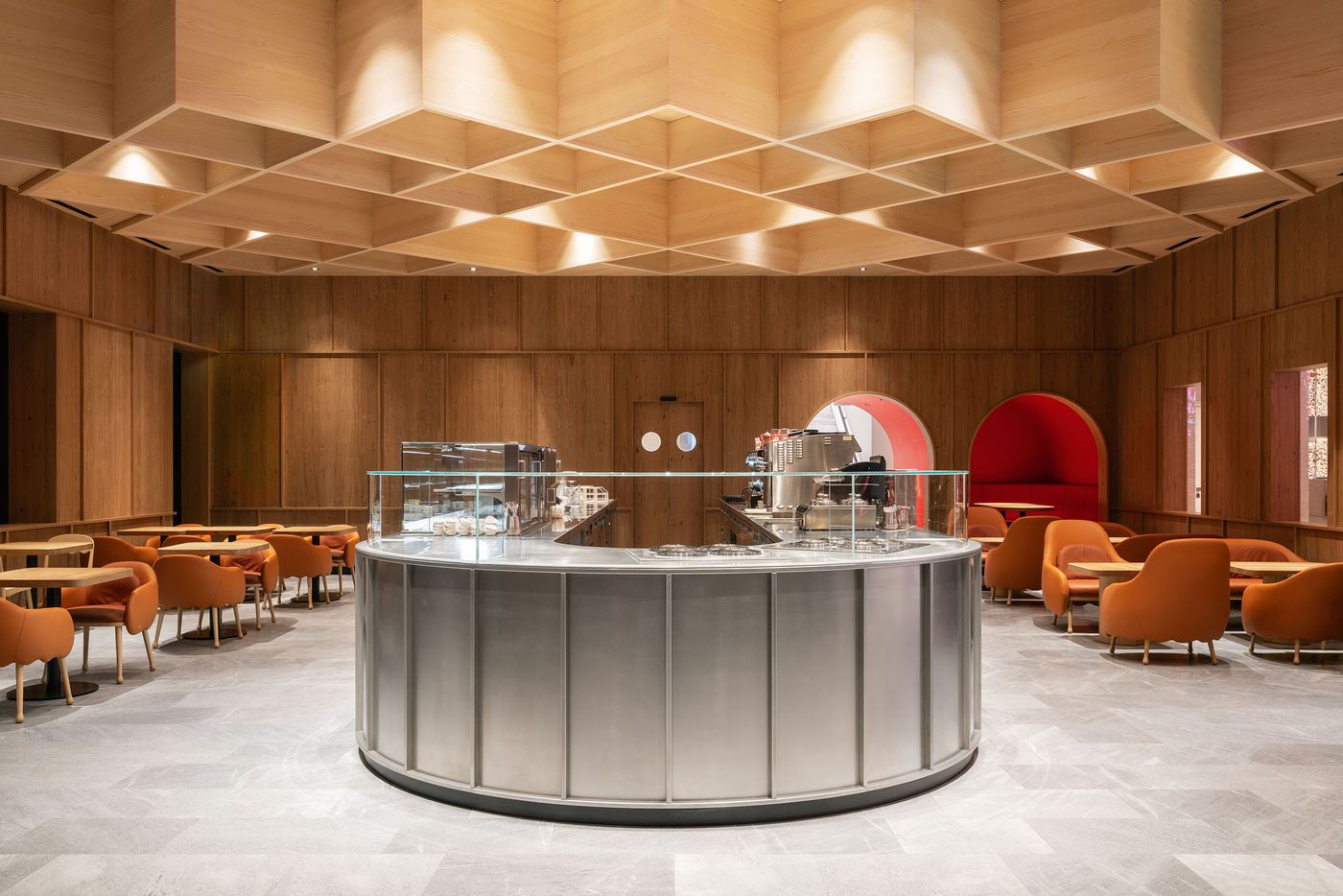 Intimate seating pods carved into timber-lined walls create contemplative alcoves within this modern café space. The geometric coffered ceiling treatment and warm orange upholstered furniture establish a cozy counterpoint to the clean architectural lines, embodying Japandi principles of functional comfort. Intimate seating pods carved into timber-lined walls create contemplative alcoves within this modern café space. The geometric coffered ceiling treatment and warm orange upholstered furniture establish a cozy counterpoint to the clean architectural lines, embodying Japandi principles of functional comfort.