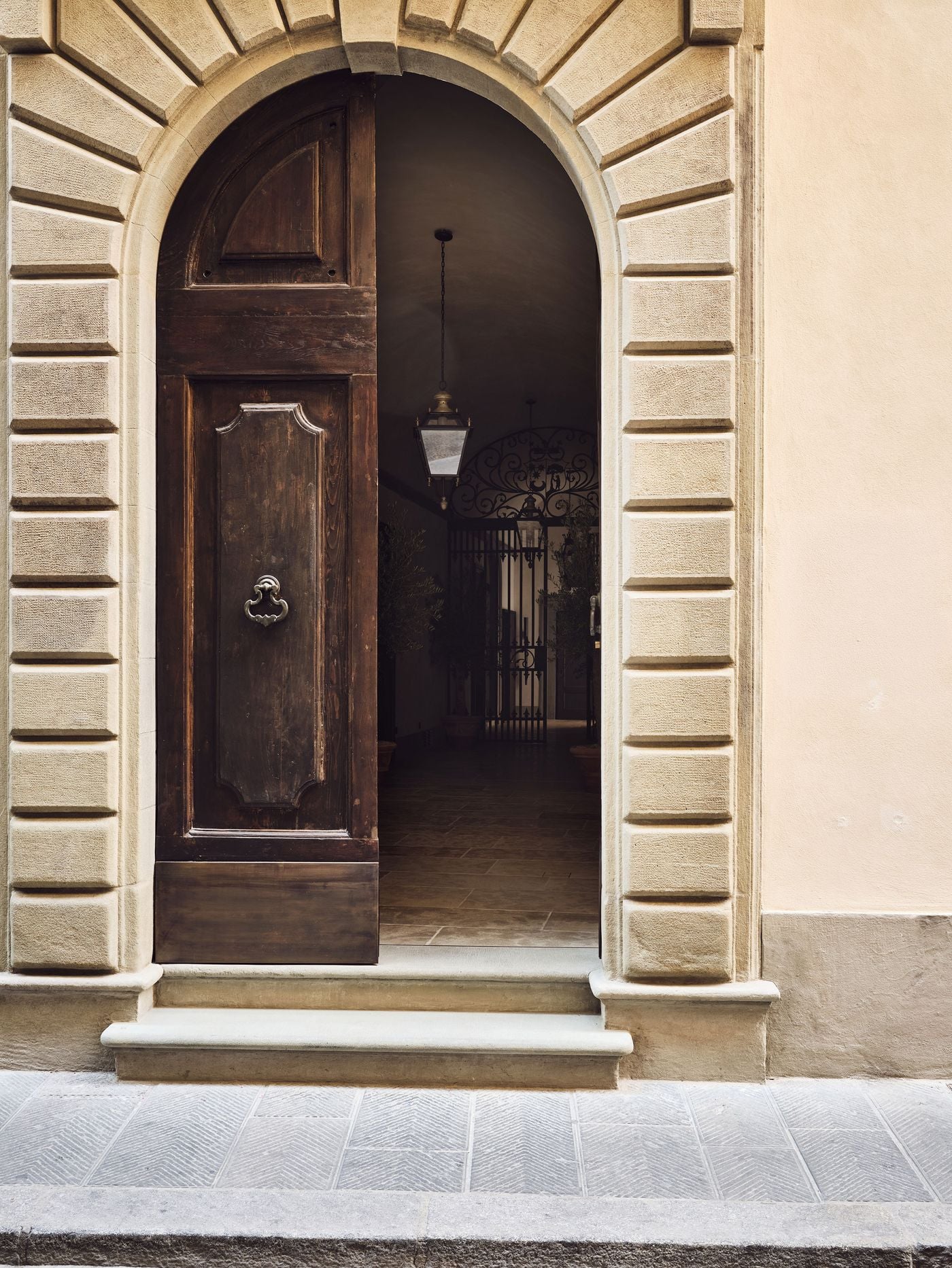 The street entrance of La Réserve Firenze on Via Santo Spirito, where a rusticated stone arch frames a weathered wooden door left ajar. A heavy iron knocker, a worn stone step and a glimpse of a glazed lantern and wrought-iron gate within hint at the quiet world beyond the threshold. The street entrance of La Réserve Firenze on Via Santo Spirito, where a rusticated stone arch frames a weathered wooden door left ajar. A heavy iron knocker, a worn stone step and a glimpse of a glazed lantern and wrought-iron gate within hint at the quiet world beyond the threshold.