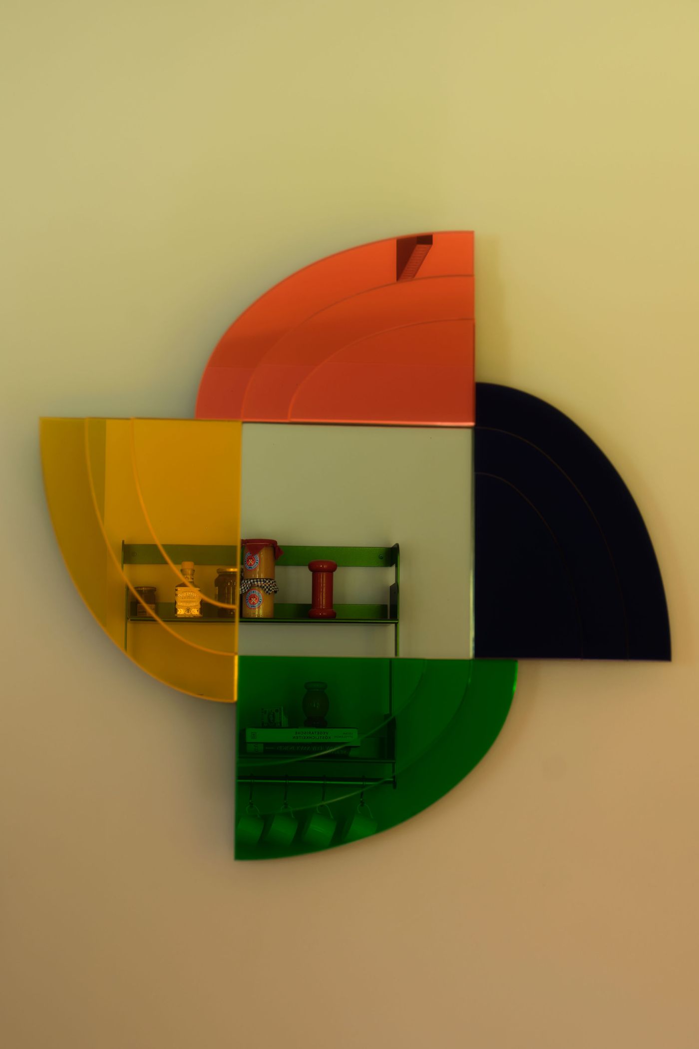A colorful, geometric wall-mounted shelf featuring curved glass in orange, yellow, black, and green, showcasing decorative items inside. A colorful, geometric wall-mounted shelf featuring curved glass in orange, yellow, black, and green, showcasing decorative items inside.