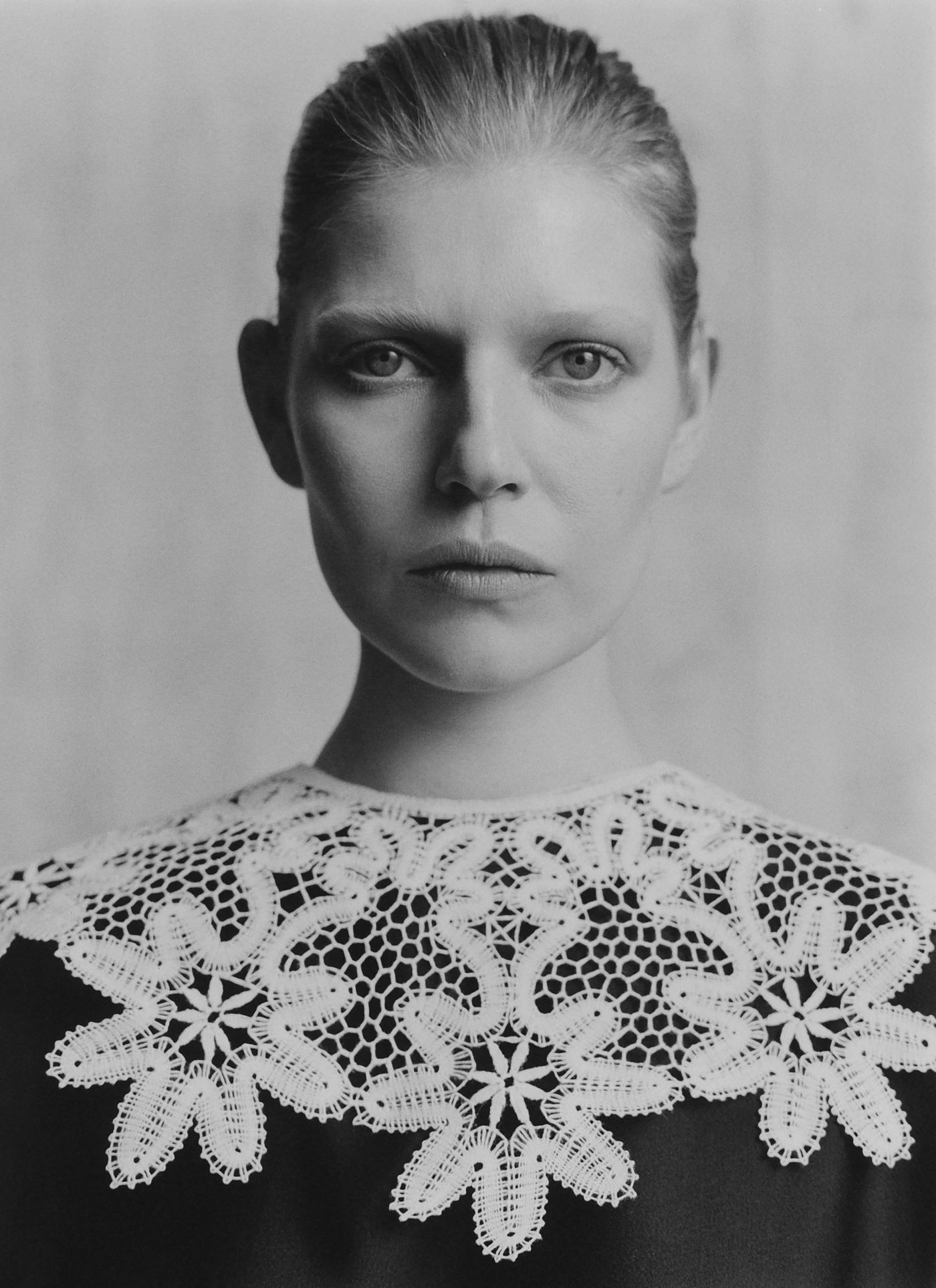 A person wearing a dark garment adorned with intricate white lace detailing on the collar.