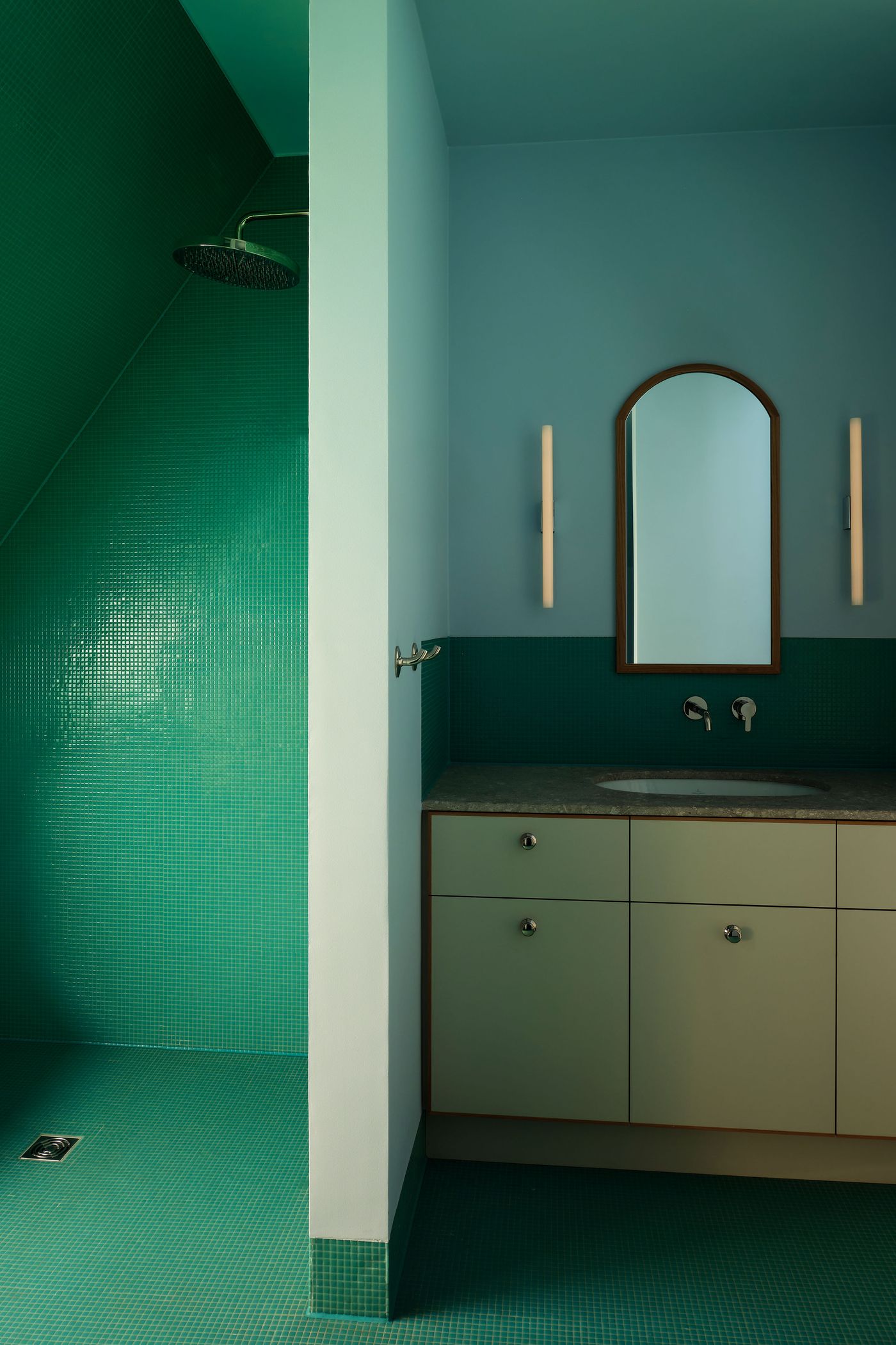 A modern bathroom featuring green tiled walls, a spacious shower, a round mirror, and a sleek countertop with a sink.