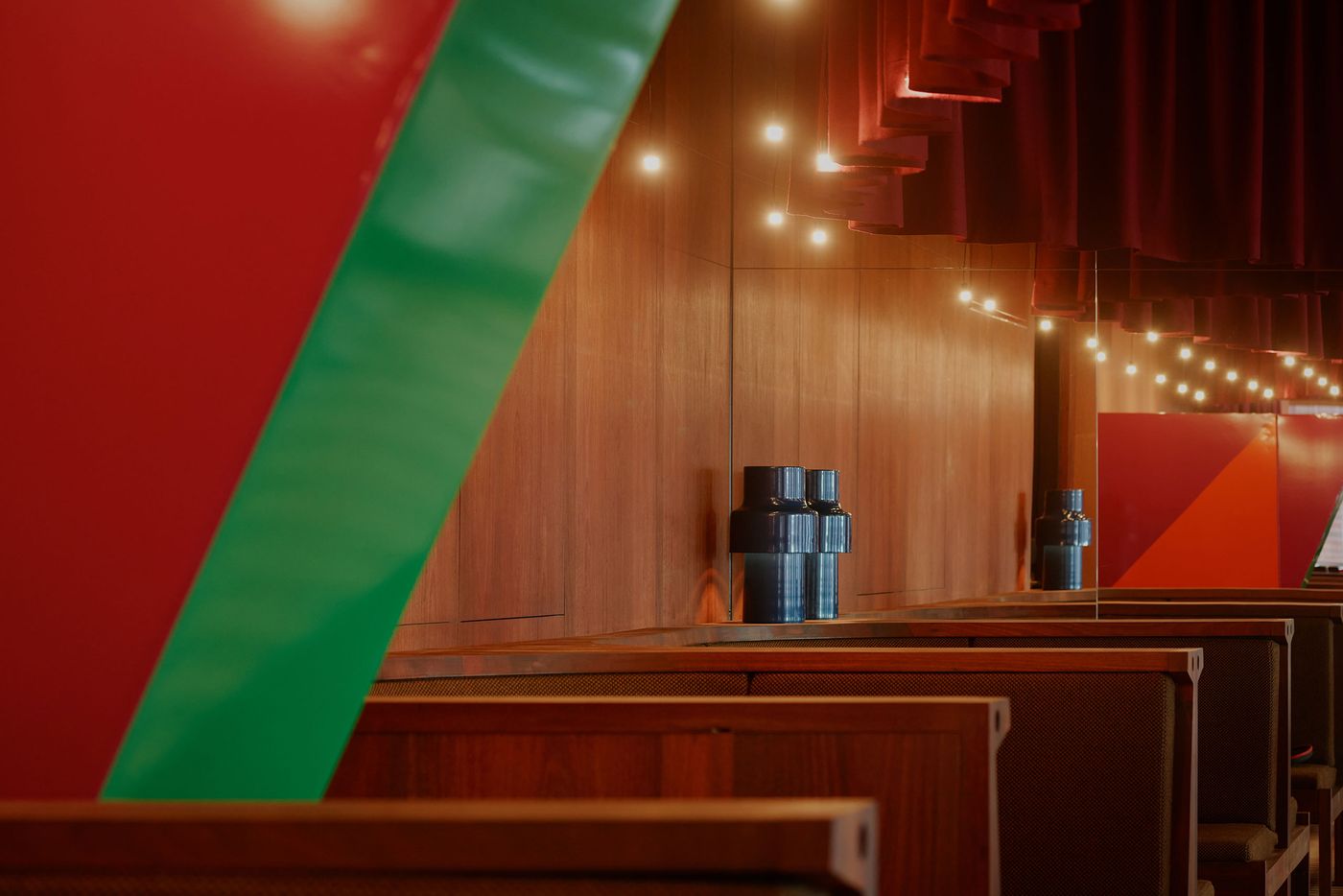 Interior of a modern space featuring wooden furnishings, a dark blue decorative vase, and vibrant red and green wall accents. Interior of a modern space featuring wooden furnishings, a dark blue decorative vase, and vibrant red and green wall accents.