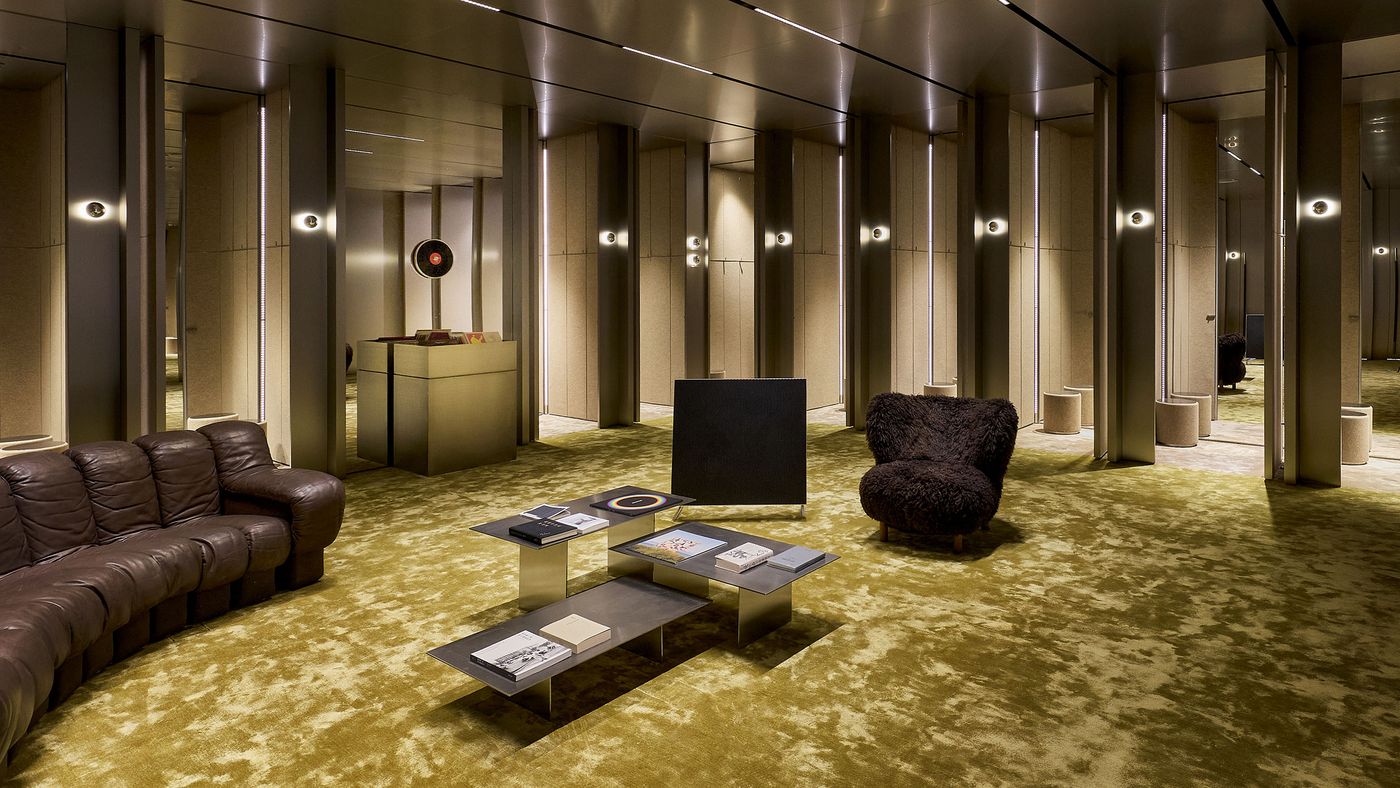 A modern lounge with a brown leather sofa, a plush chair, sleek coffee table with books, and ambient lighting in a stylish, textured space. A modern lounge with a brown leather sofa, a plush chair, sleek coffee table with books, and ambient lighting in a stylish, textured space.