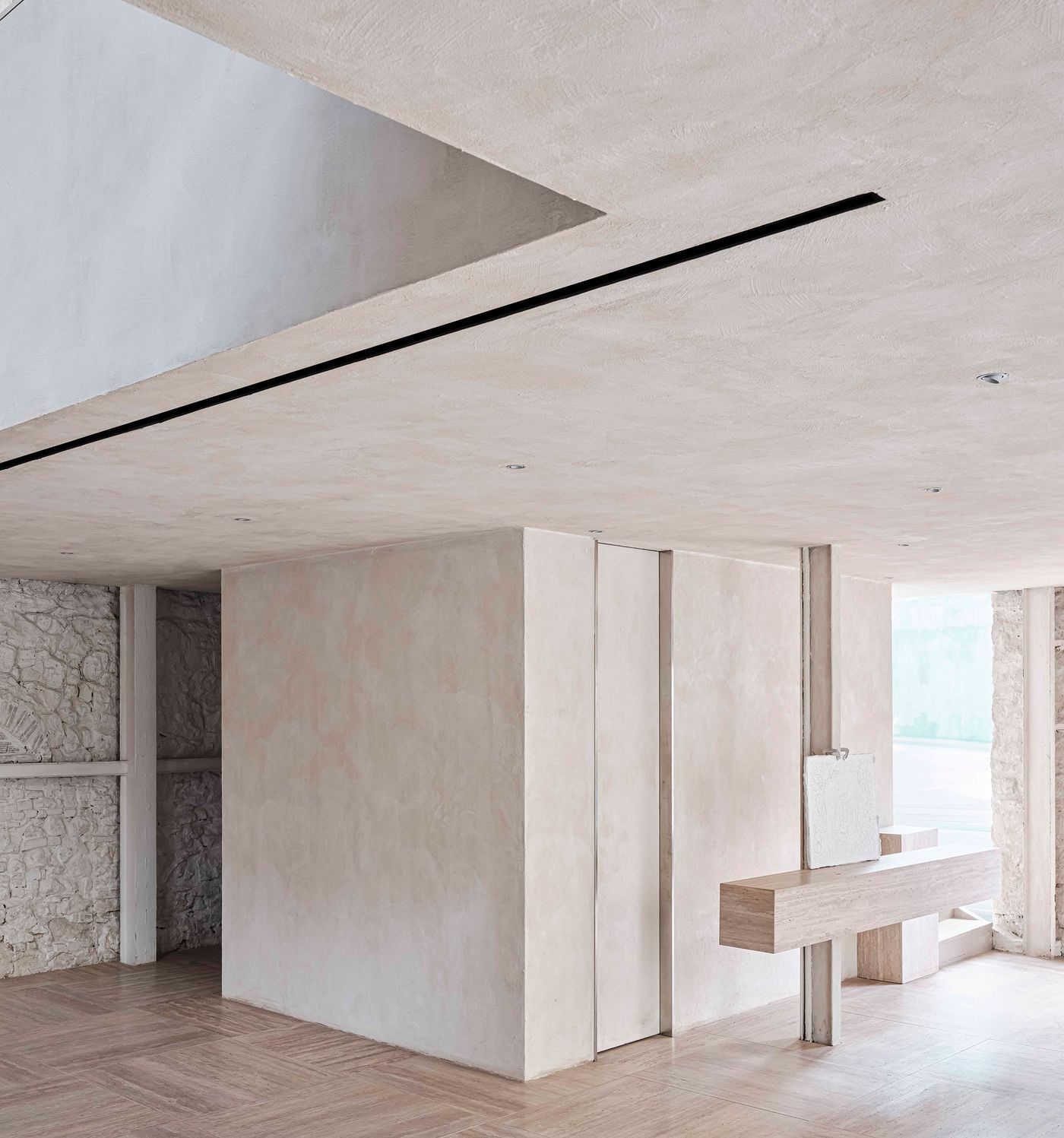 A pale, monolithic volume sits within Castor Place’s retained masonry shell, its softly mottled plaster contrasting with the rough stonework visible around it. A slender travertine display ledge projects from a structural post, while recessed spotlights and a linear ceiling slot reinforce the restrained architectural language. A pale, monolithic volume sits within Castor Place’s retained masonry shell, its softly mottled plaster contrasting with the rough stonework visible around it. A slender travertine display ledge projects from a structural post, while recessed spotlights and a linear ceiling slot reinforce the restrained architectural language.