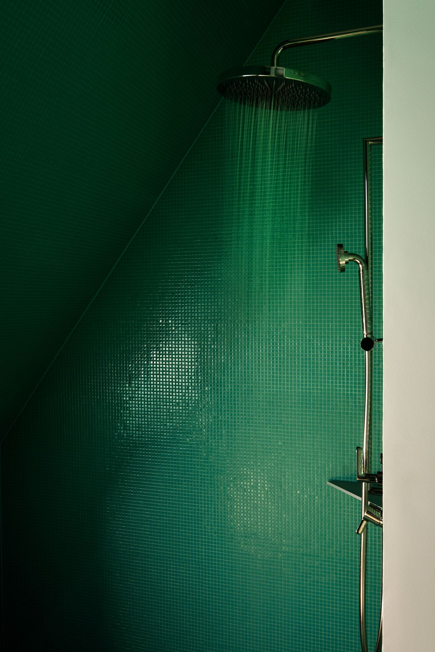 A modern shower with a rain showerhead, water cascading down green tiled walls in a geometric design.