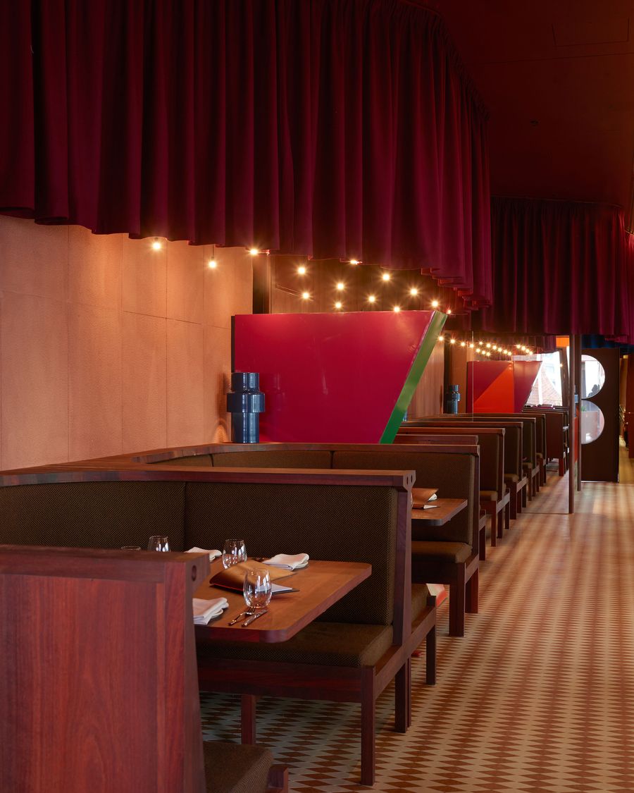 Interior of a stylish restaurant featuring wooden booths, dim lighting, and vibrant red decor elements against a textured wall. Interior of a stylish restaurant featuring wooden booths, dim lighting, and vibrant red decor elements against a textured wall.