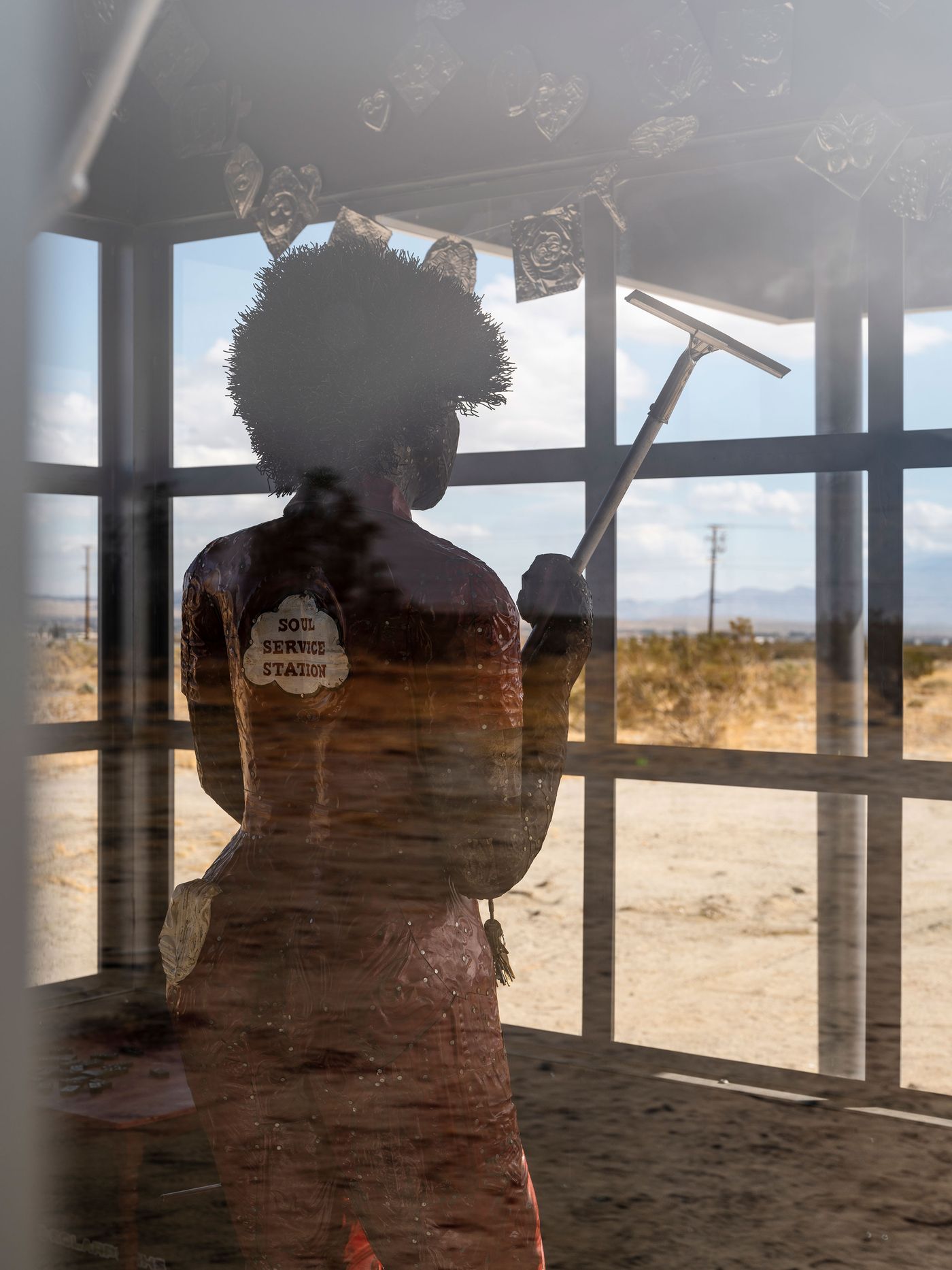 A silhouette of a figure cleaning a window, wearing a red outfit labeled "Soul Service Station," framed by desert landscape.