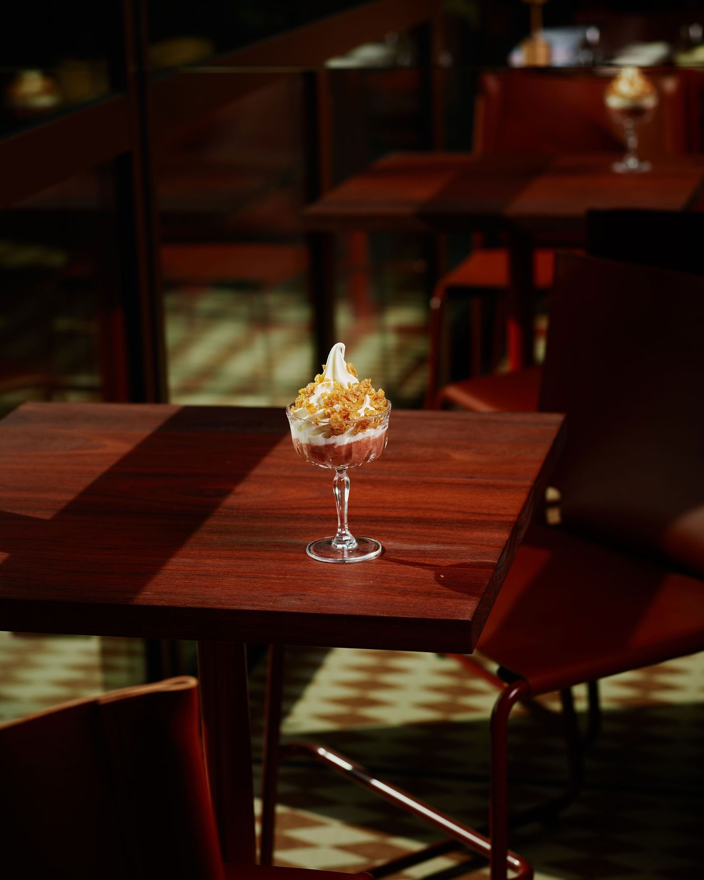 A glass dessert topped with popcorn sits on a wooden table in a warmly lit café, showcasing cozy dining ambiance.
