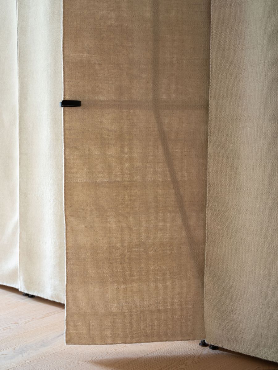 A close-up of a silky, tan curtain hanging partially open, revealing soft textures and a sleek black clip on its edge. A close-up of a silky, tan curtain hanging partially open, revealing soft textures and a sleek black clip on its edge.